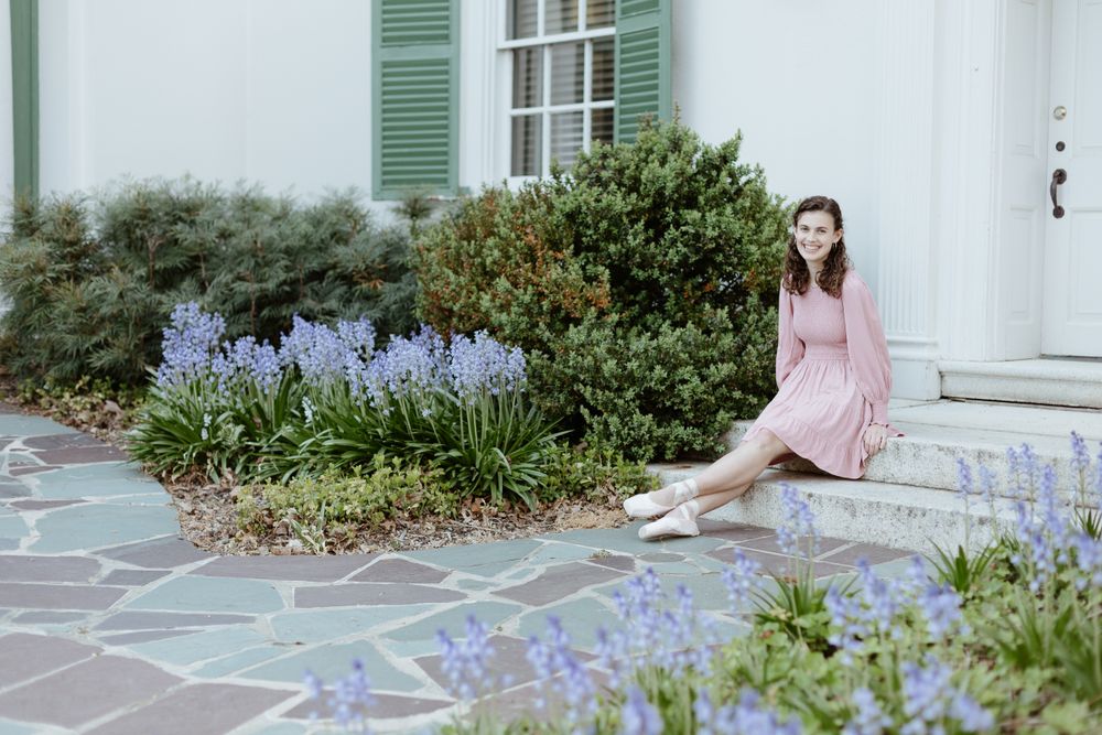 Dancer in pink dress poses gracefully among spring garden flowers.