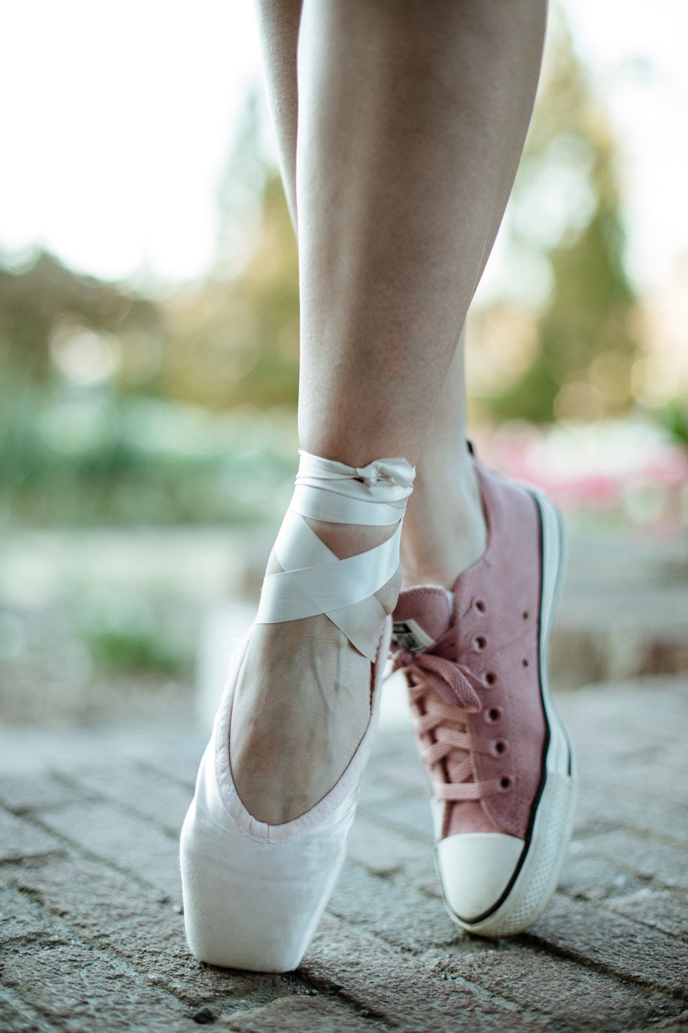Contrast of ballet pointe shoe and pink sneaker on stone surface.