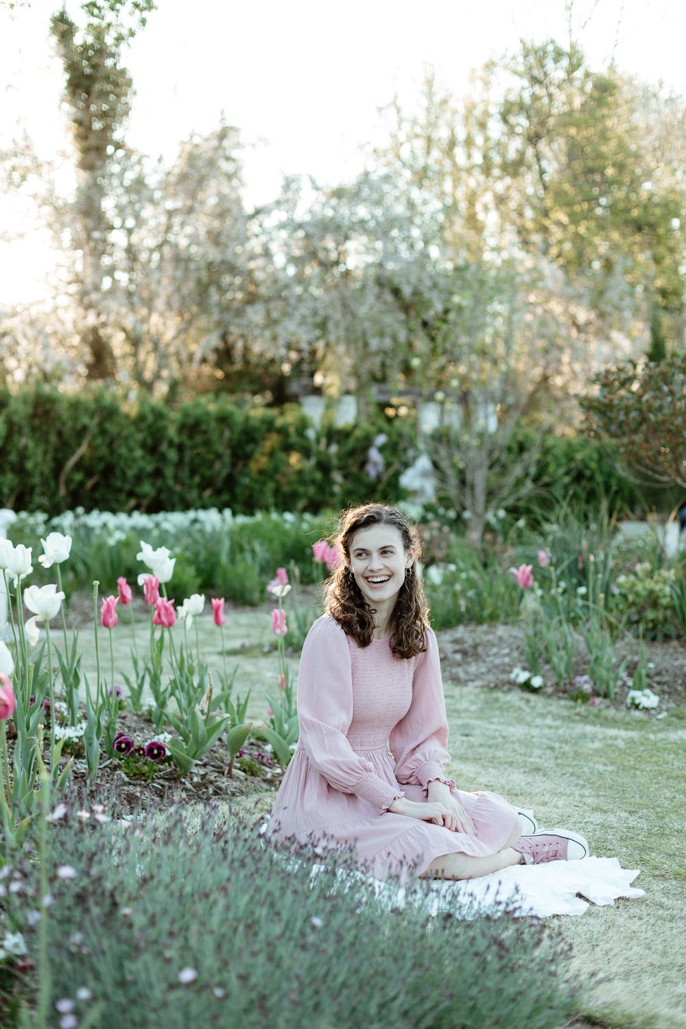 Spring garden photoshoot featuring pink dress against blooming flowers and greenery.