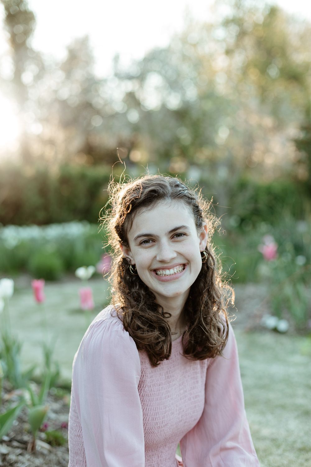Soft springtime portrait in pink sweater amid blooming garden setting.
