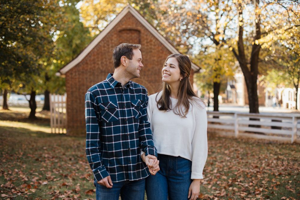 Couple sharing romantic moments during fall photo session near white fence and brick buildings.