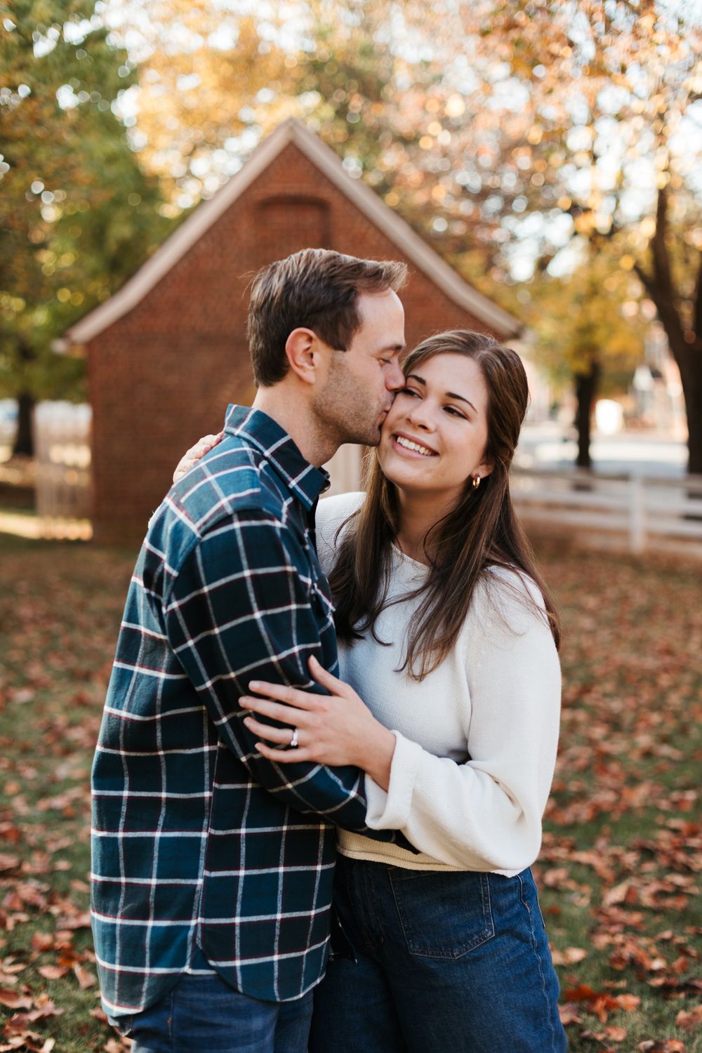 Autumn engagement photos with couple in plaid and white sweater by brick buildings.