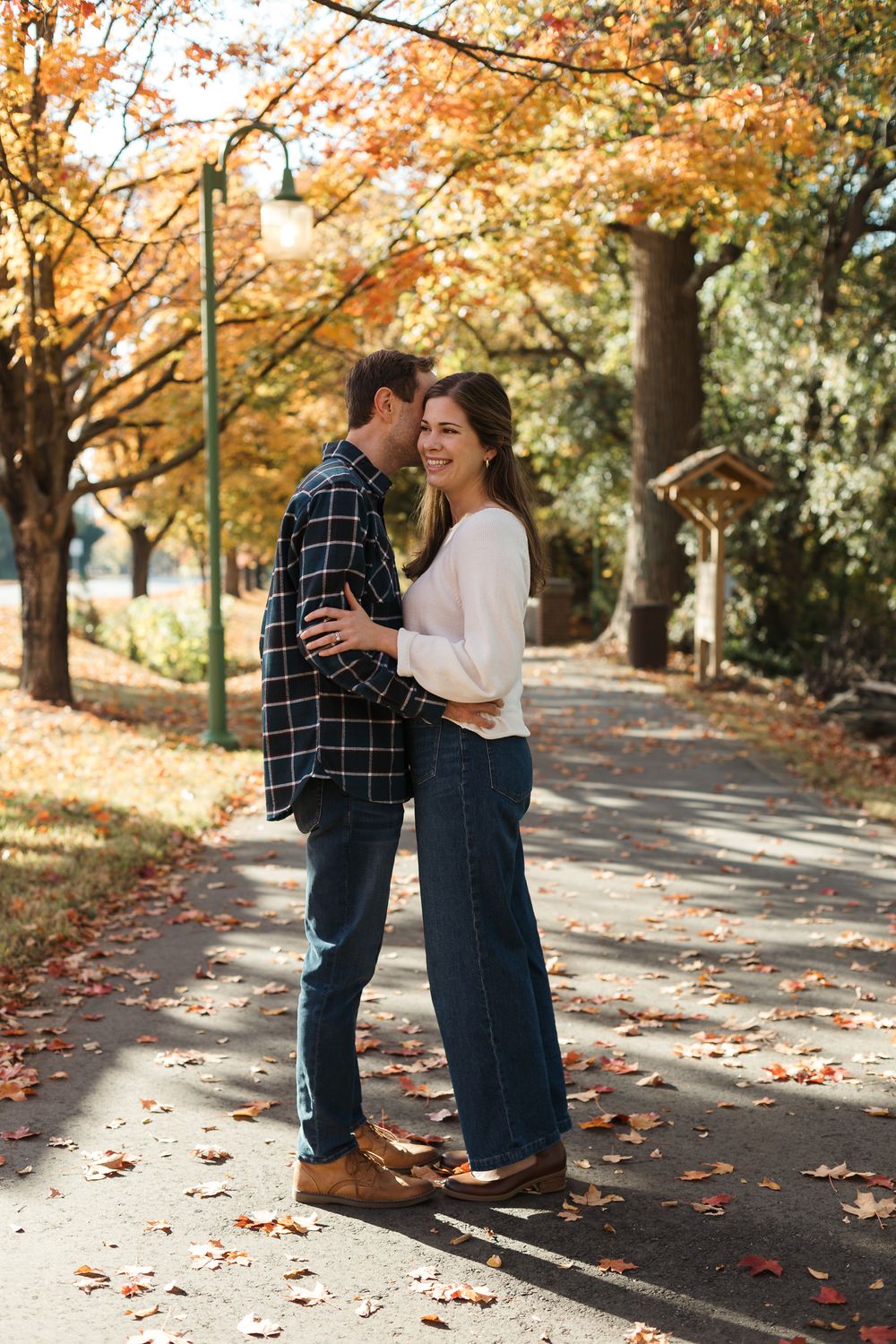 Couple embracing on leaf-covered path during autumn photoshoot with golden trees.
