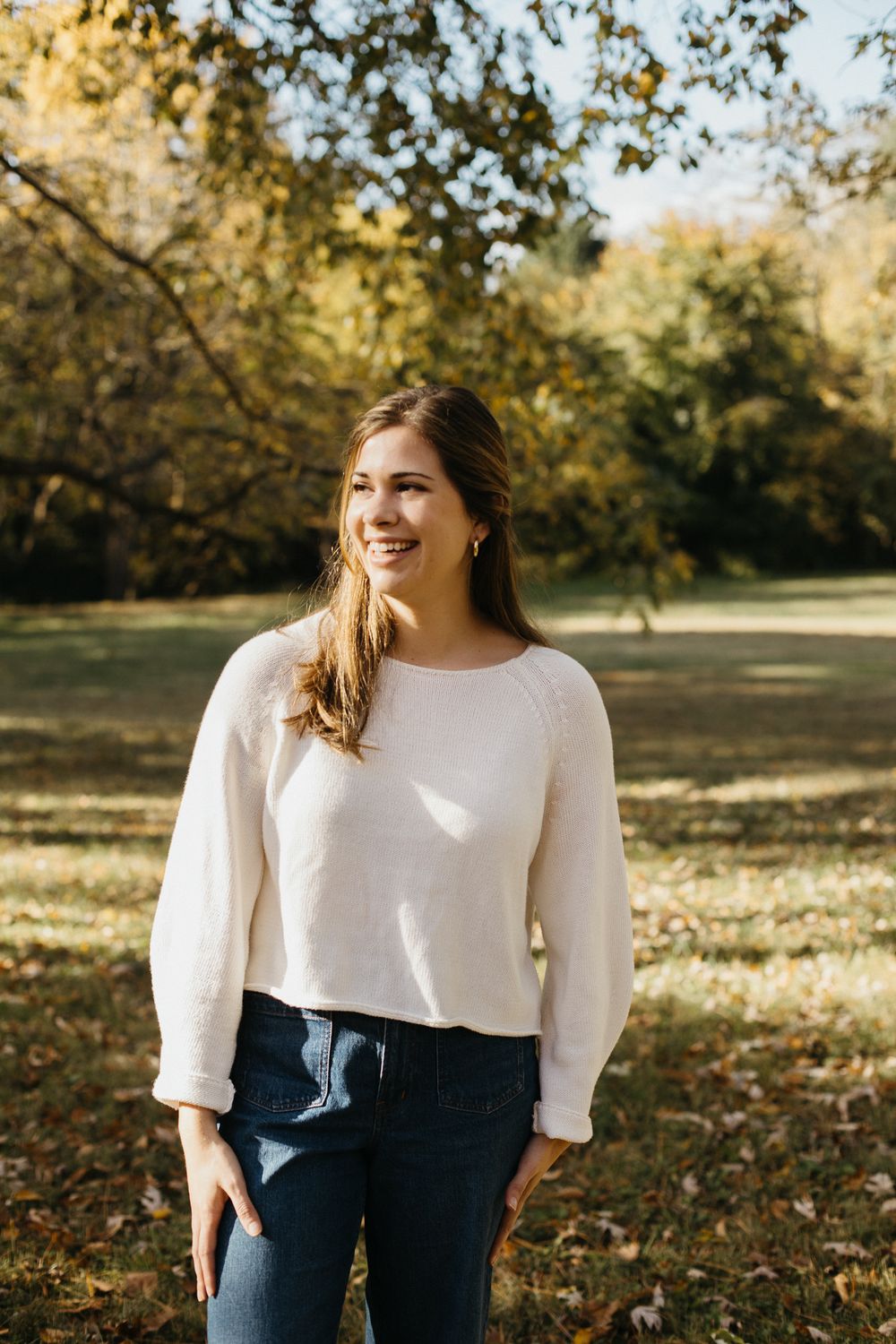 Woman in white sweater smiling during autumn outdoor photoshoot.