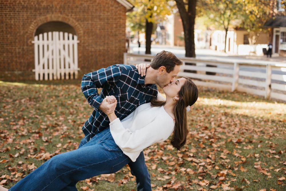 Playful engagement photos with couple near brick building and white fence in autumn.