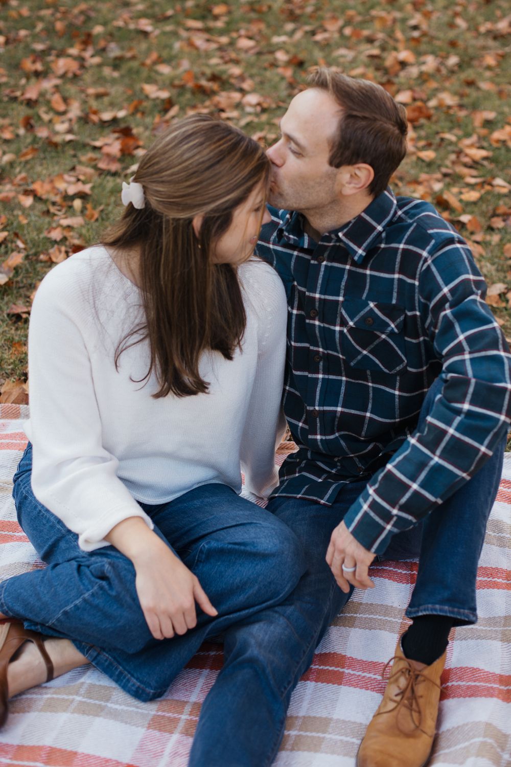 Romantic couple shares intimate moments on a plaid blanket surrounded by fall foliage.