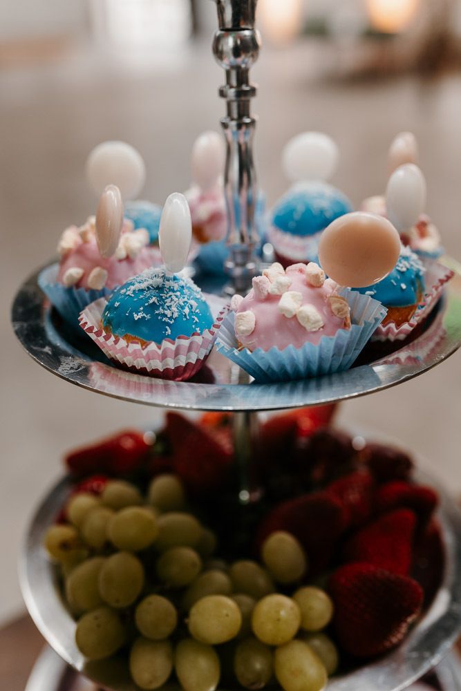 Decorative tiered stand with colorful blue and pink frosted cupcakes, grapes, and strawberries.