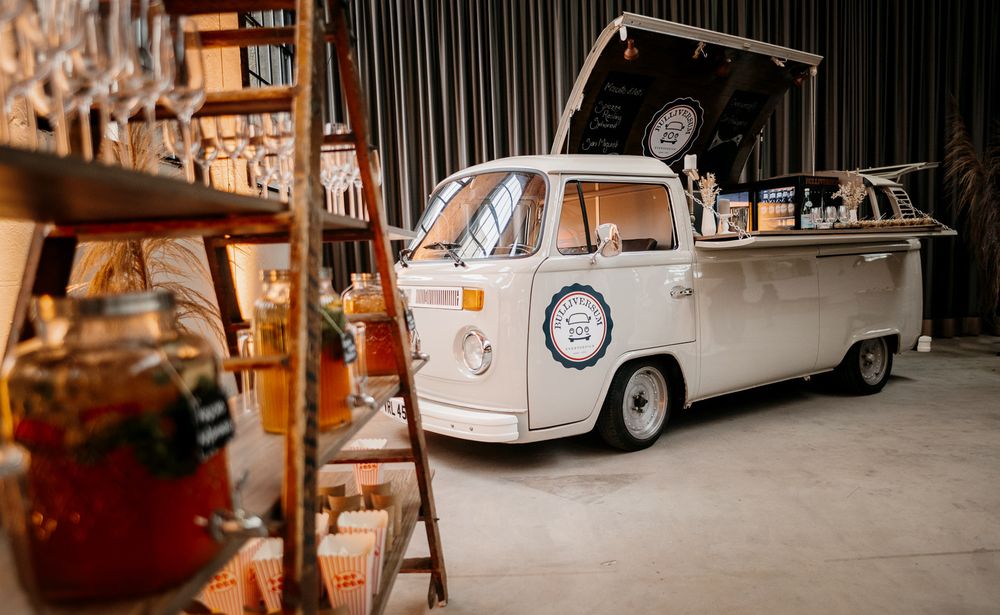 A vintage white VW camper van converted into a mobile bar setup at an indoor event venue.