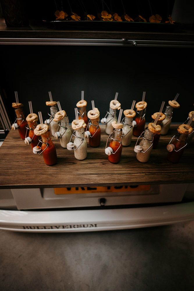 Rows of small bottled cocktails with straws displayed on a wooden shelf of a VW camper bar.