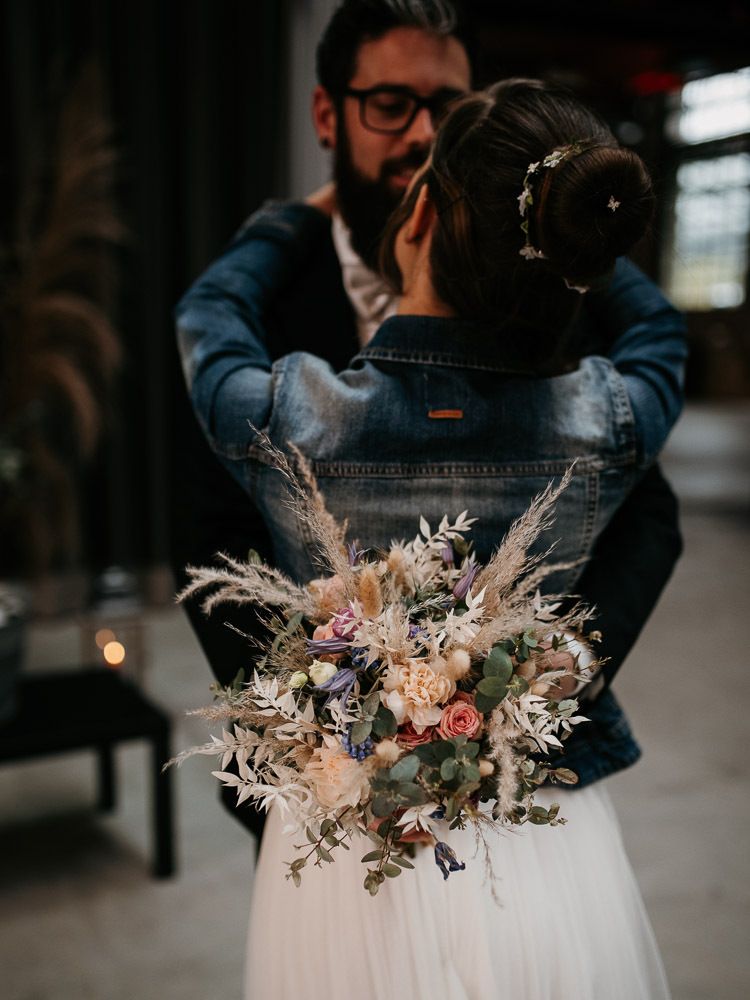 A couple embracing at their wedding, the bride holding a beautiful dried flower bouquet.