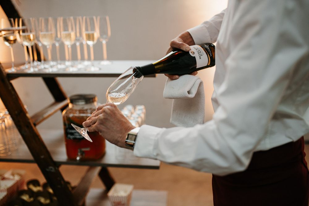 A waiter pouring champagne into a glass at an elegant wedding reception.