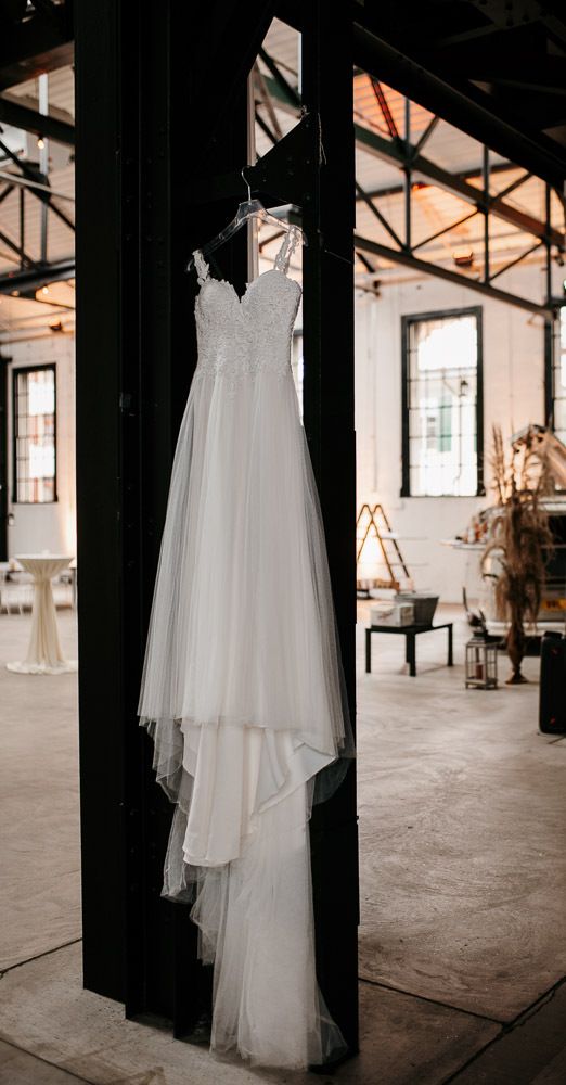 Elegant white lace wedding dress hanging on a black beam in a bright industrial venue.