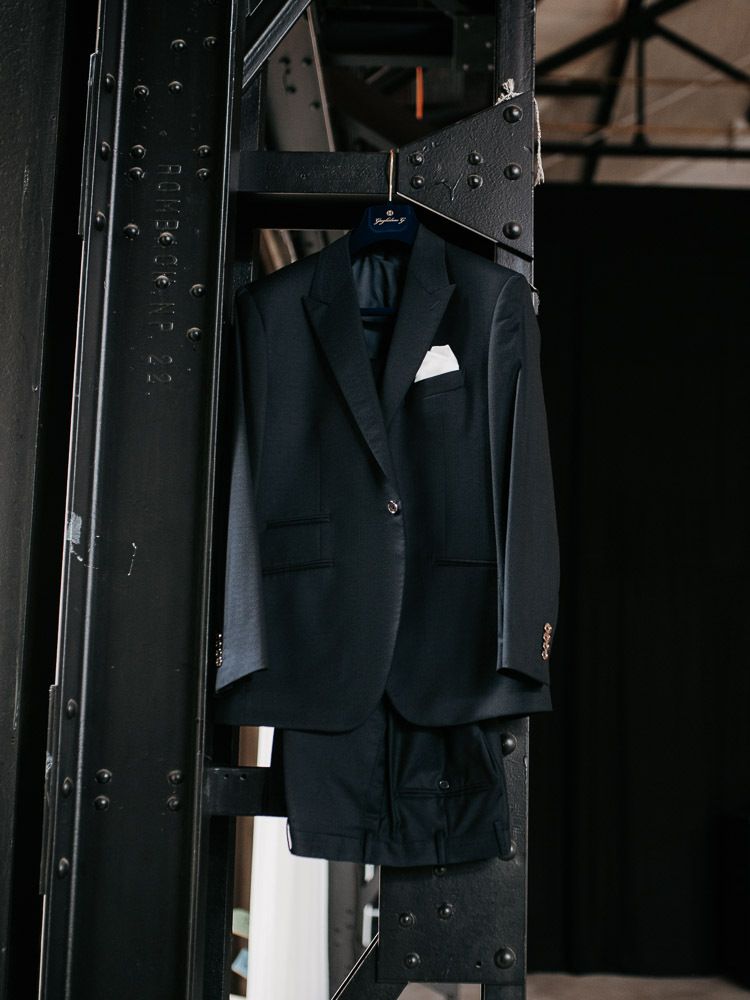 Dark navy blue suit jacket with white pocket square hanging on a black metal structure.