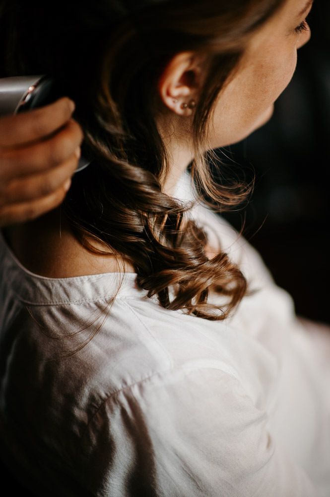 Close-up of a bride's elegant braided updo hairstyle with soft curls against a white blouse.