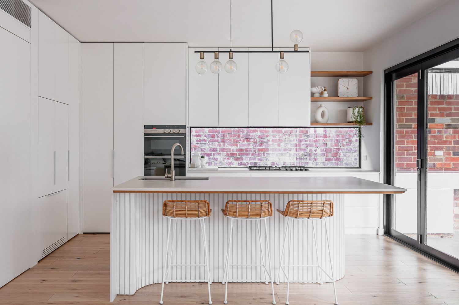 Modern white kitchen with ribbed island, wooden bar stools, and floor-to-ceiling cabinets.