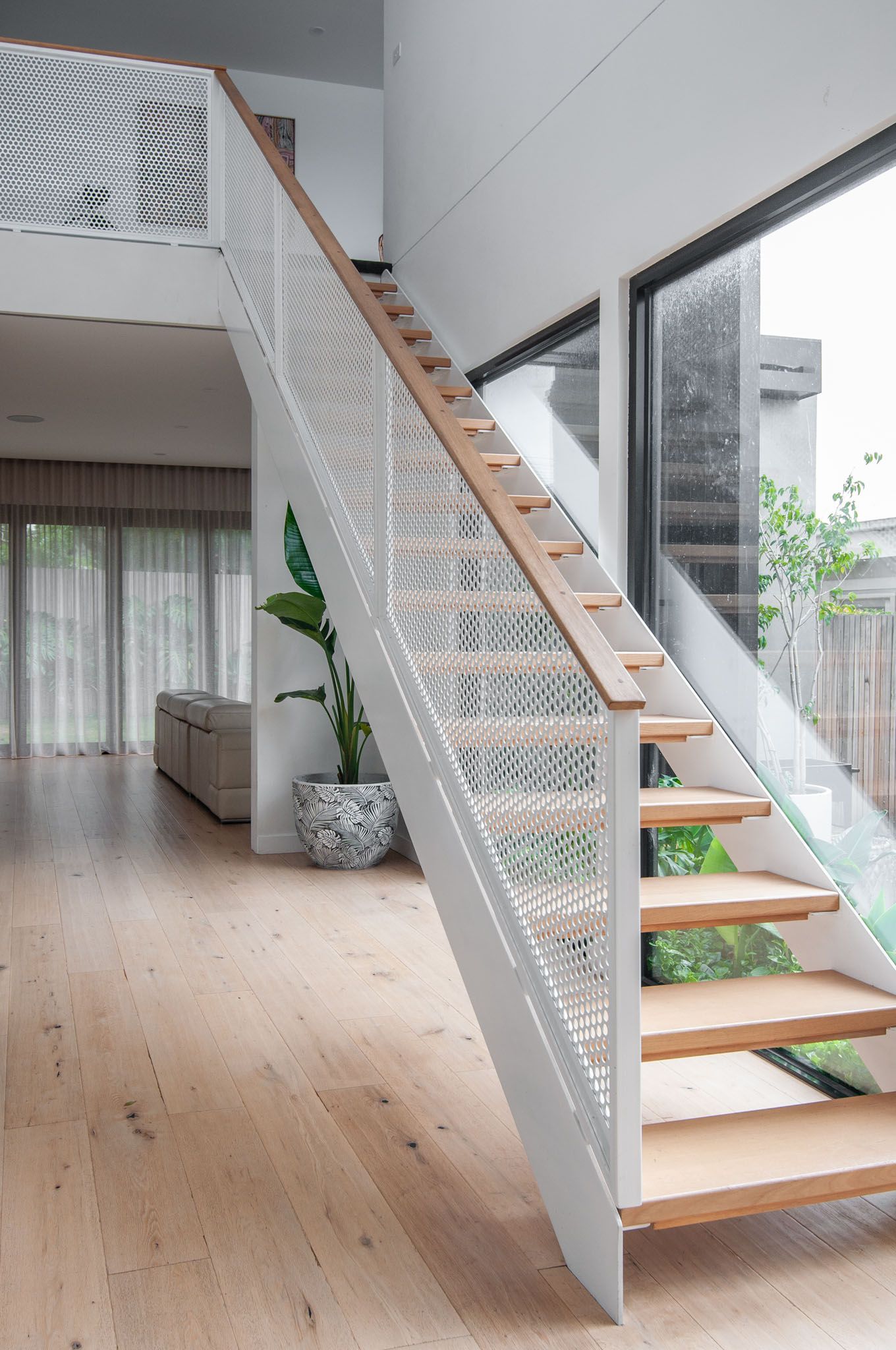 Modern staircase with wooden treads and white mesh railing in bright interior space.