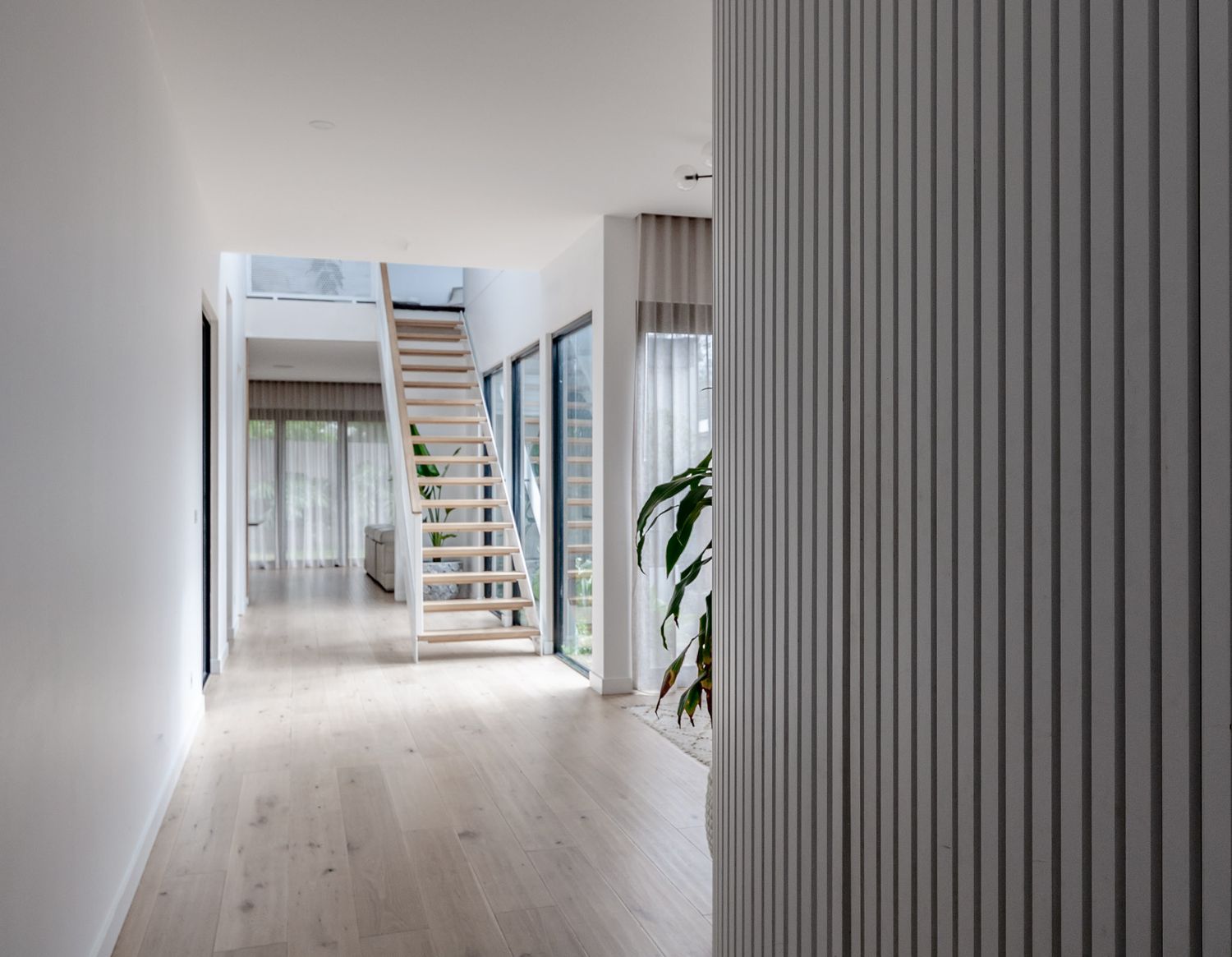 White hallway with wooden staircase and vertical grey wall panels in contemporary home design.