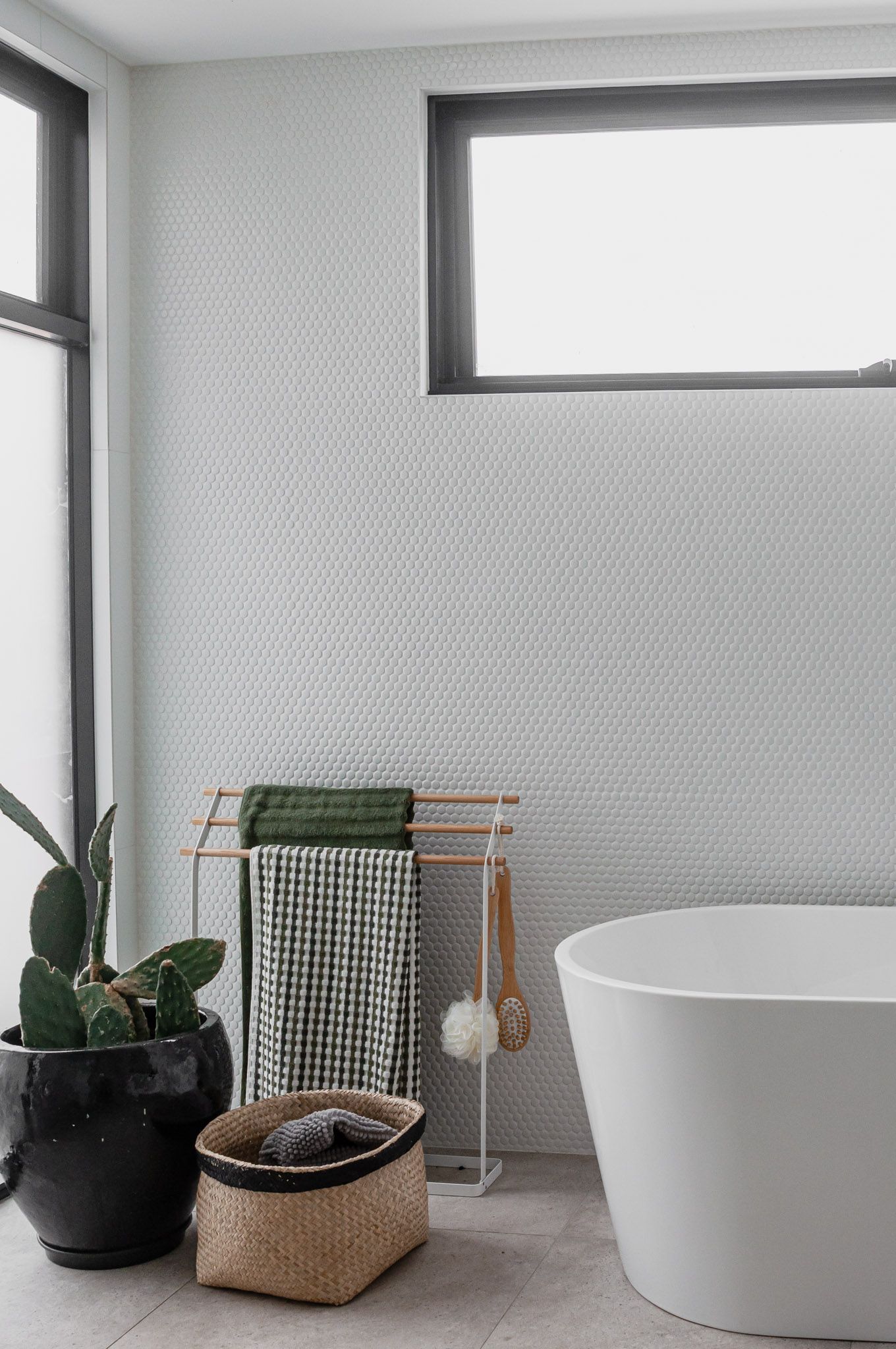 Modern bathroom featuring freestanding tub, towel rack, and potted plant against textured wall.