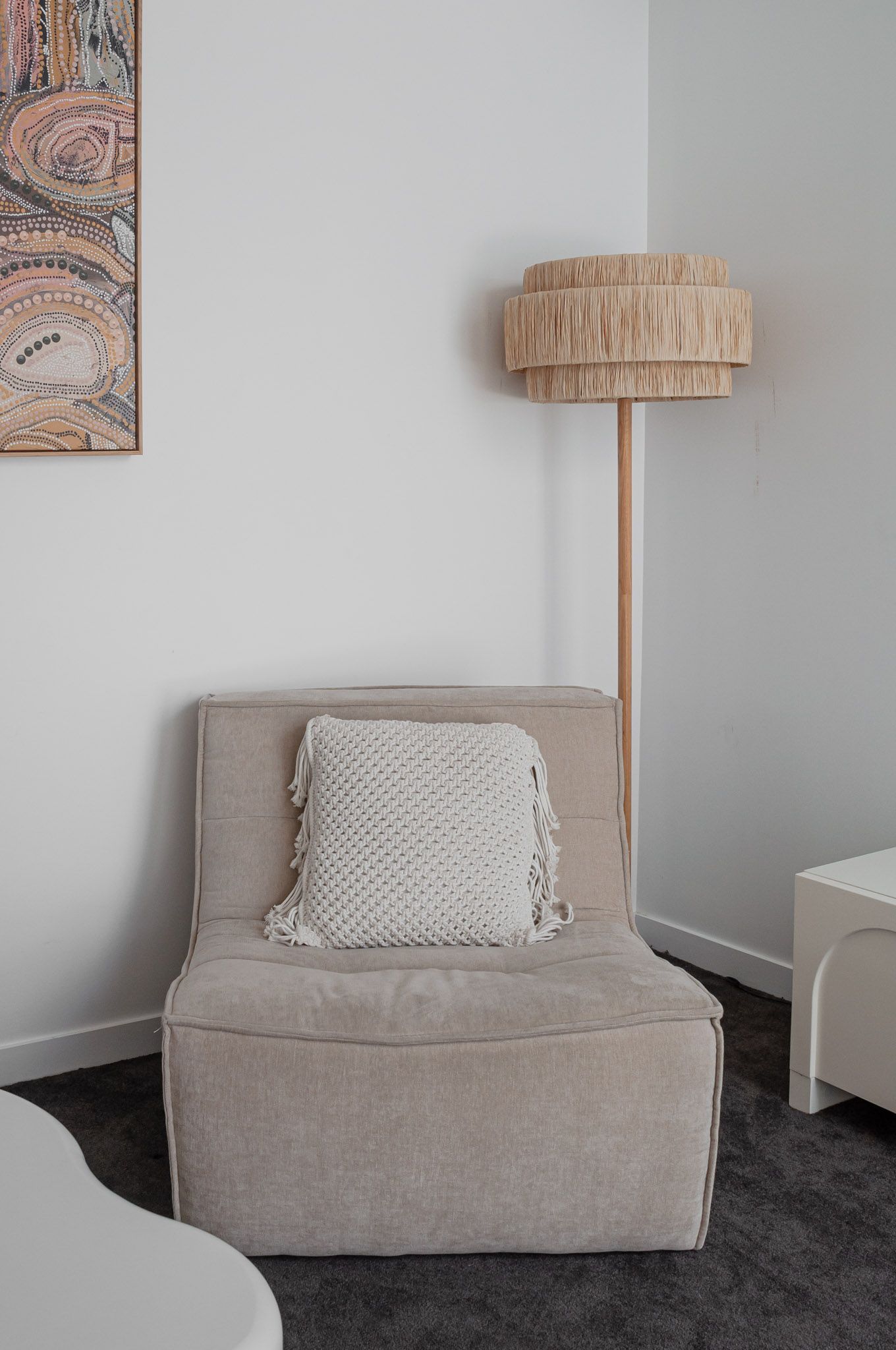 Grey accent chair with textured pillow and natural wood floor lamp in minimalist corner setting.