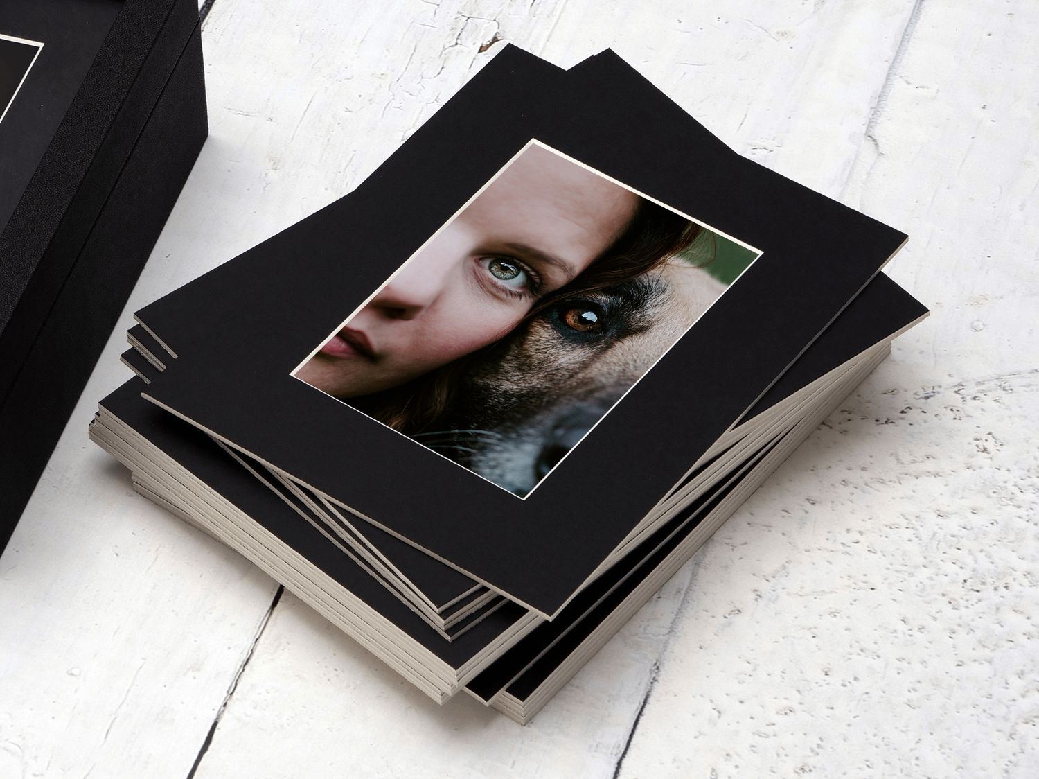Black matted photography prints stacked on white surface.