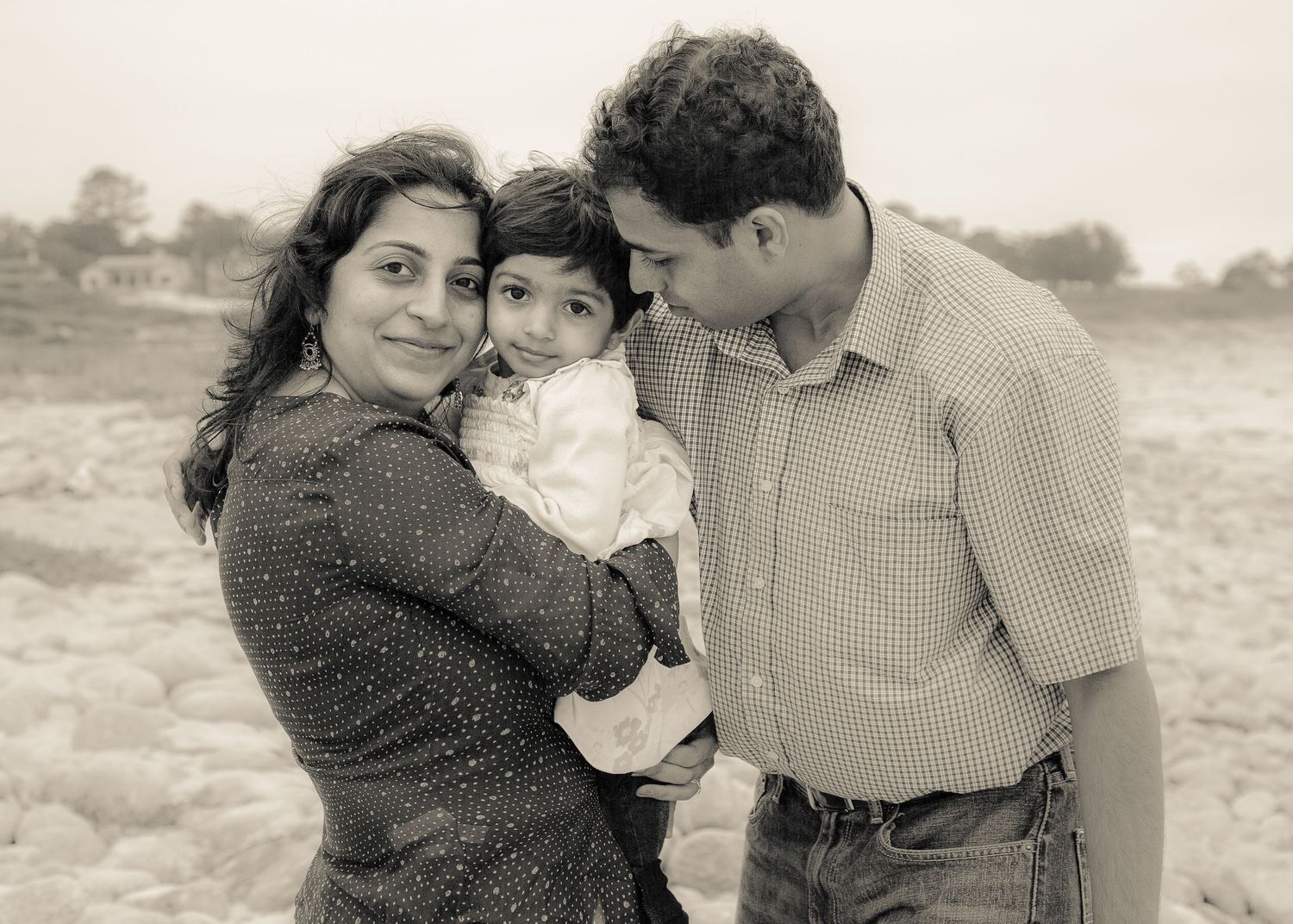Black and White photo of Young Indian family of three with 2 year girl. They are smiling and softly interacting
