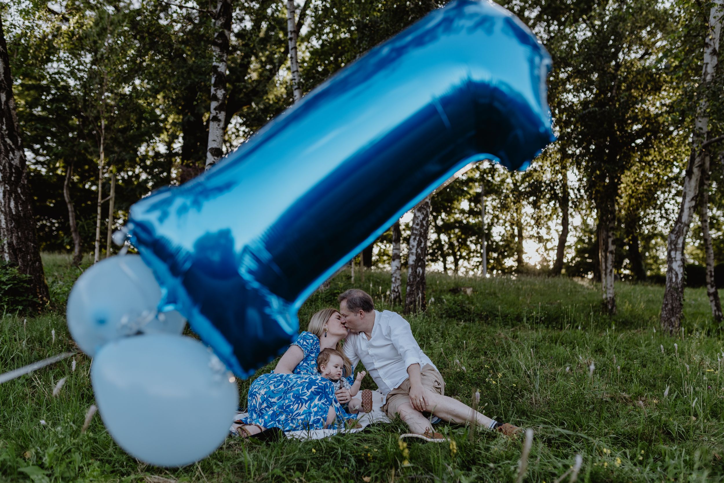 Candid photo of a family of three, smiling and enjoying time together on a blanket during a photoshoot.