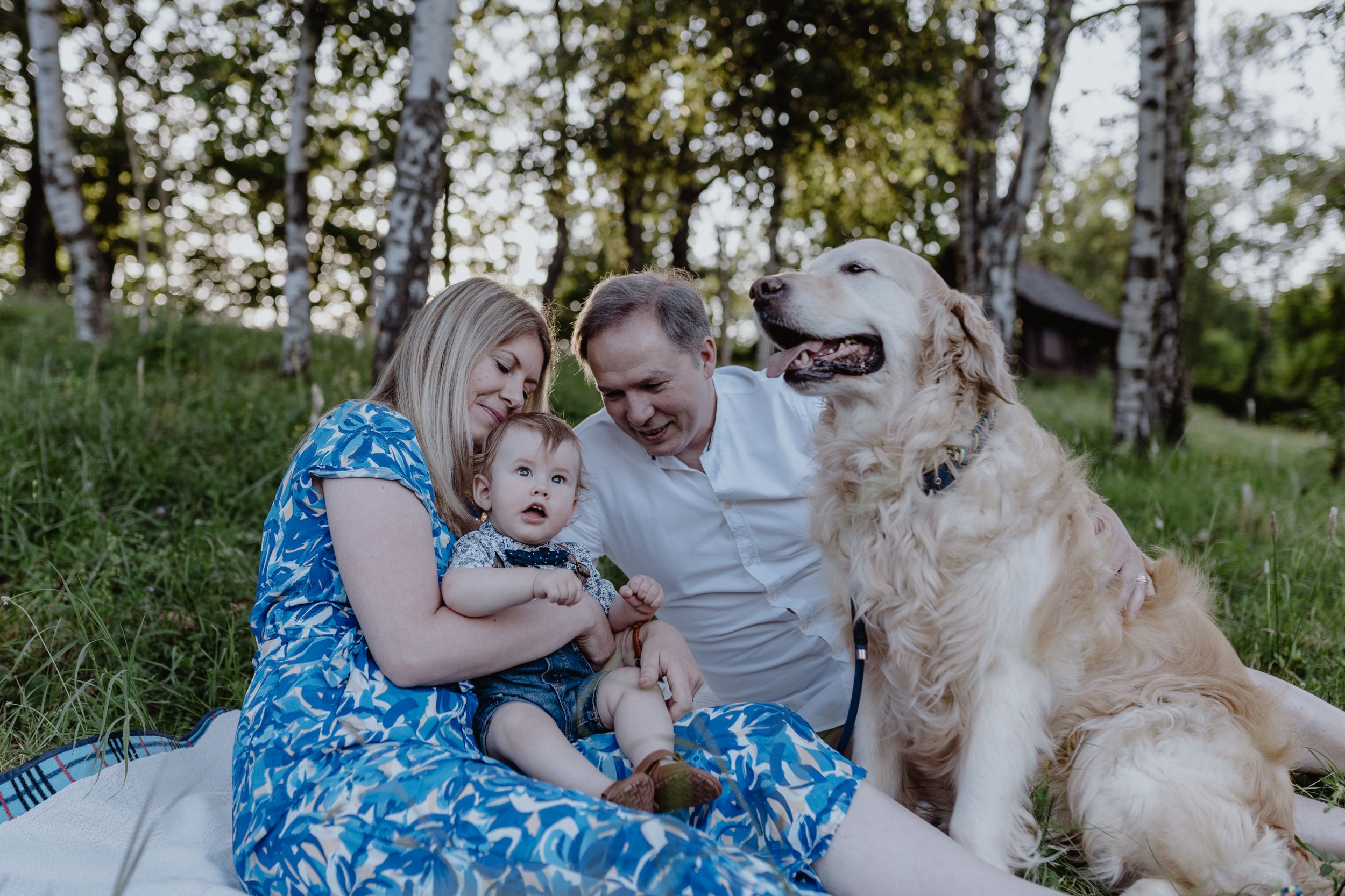 Family cuddling on a picnic blanket during a first birthday session at Jelenovac, Zagreb.