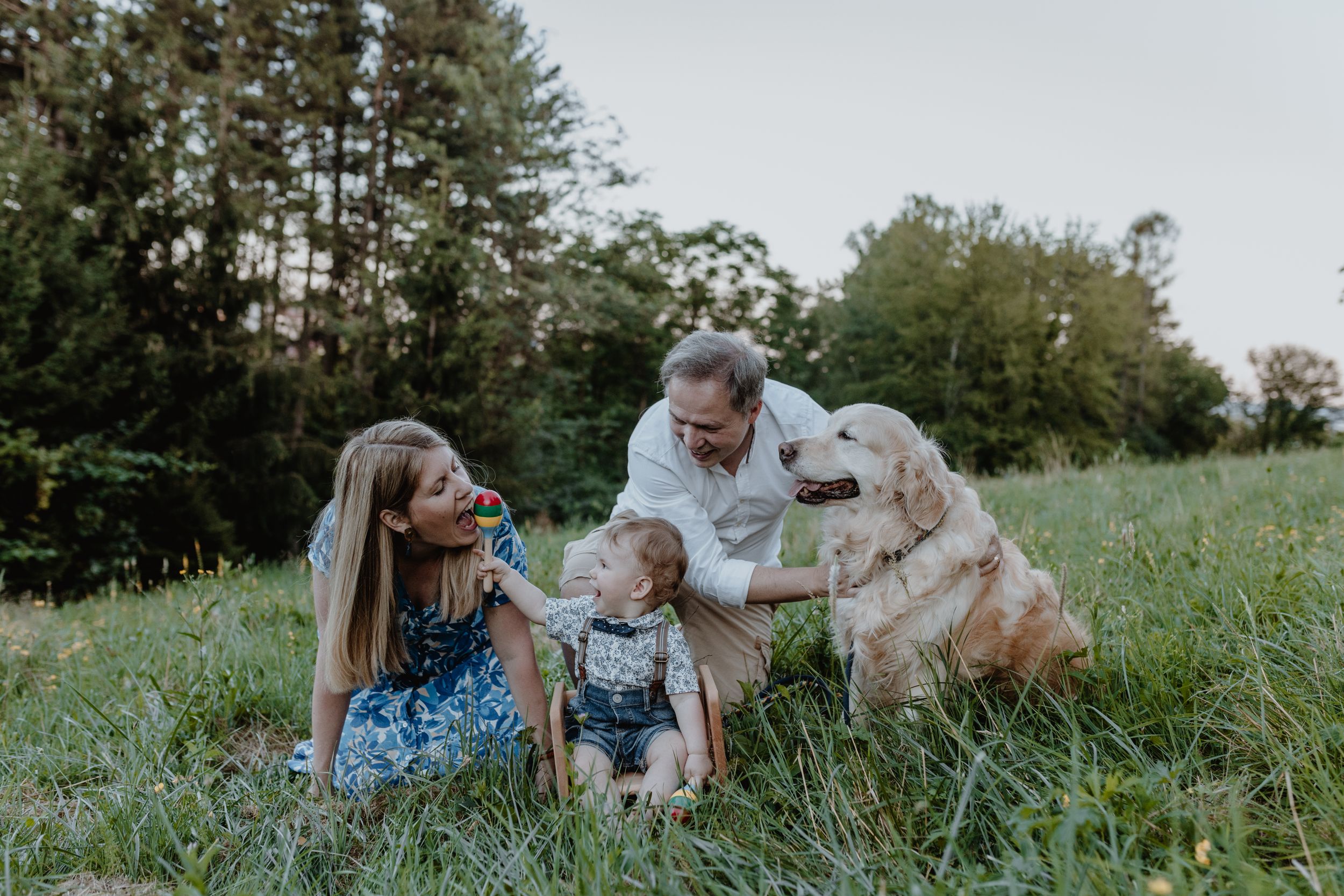 Parents, baby, and dog engaging with a colorful toy during a first birthday photoshoot at Jelenovac.