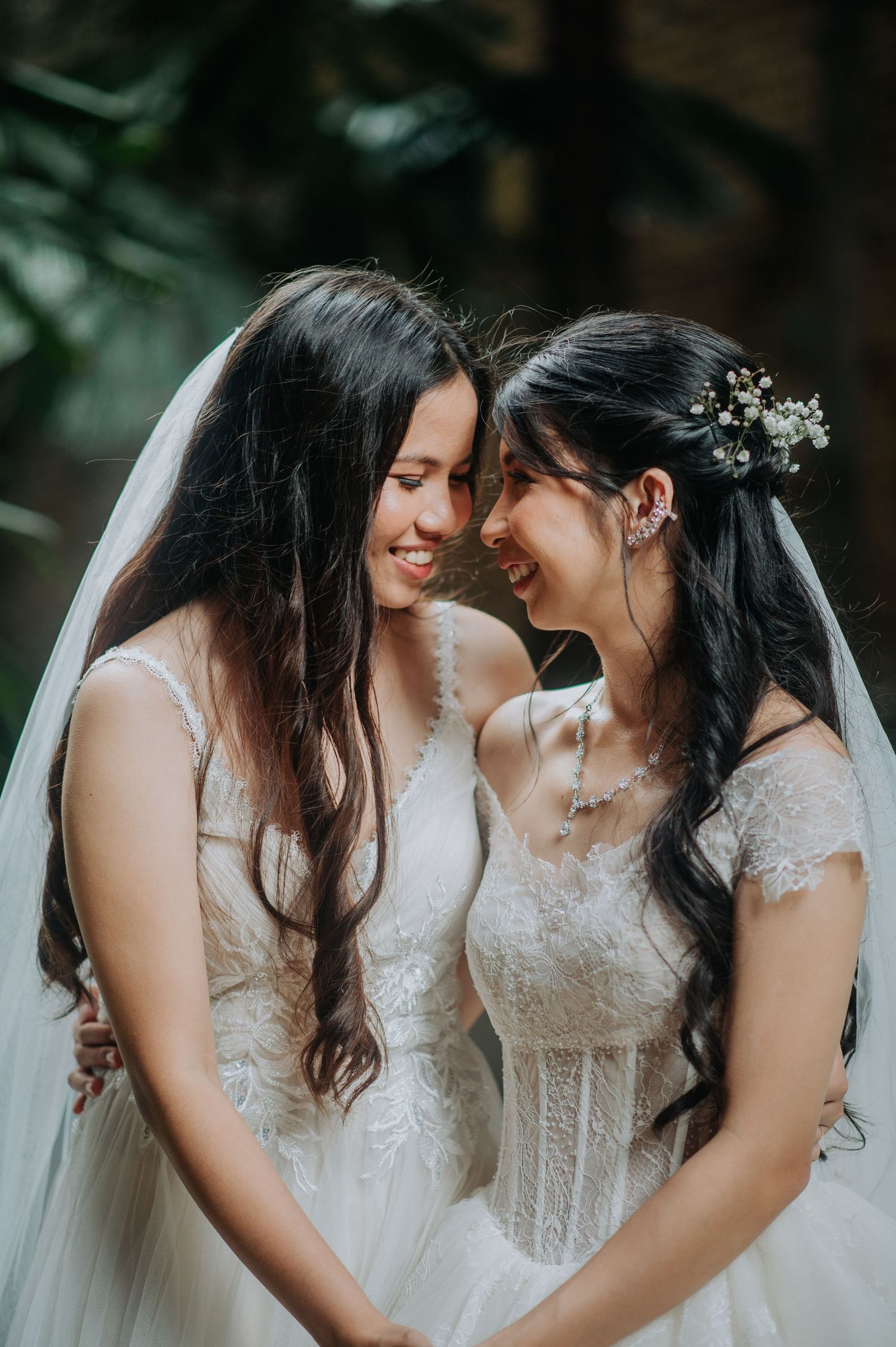 Two brides in white lace wedding dresses sharing an intimate moment outdoors.