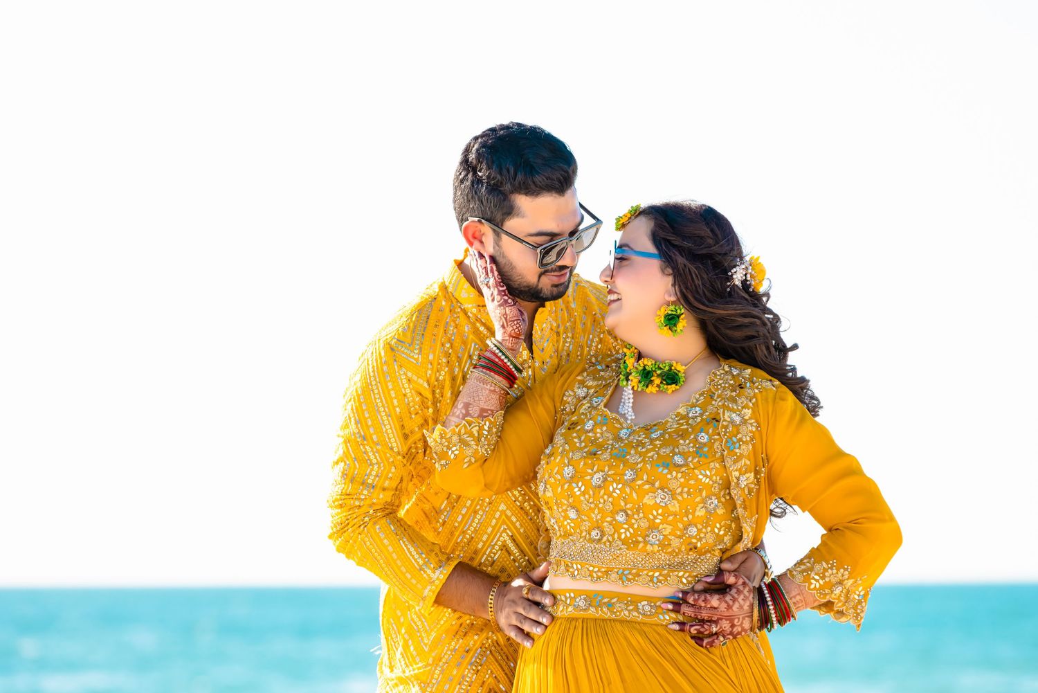 Couple in matching yellow outfits sharing a romantic moment against blue ocean background.