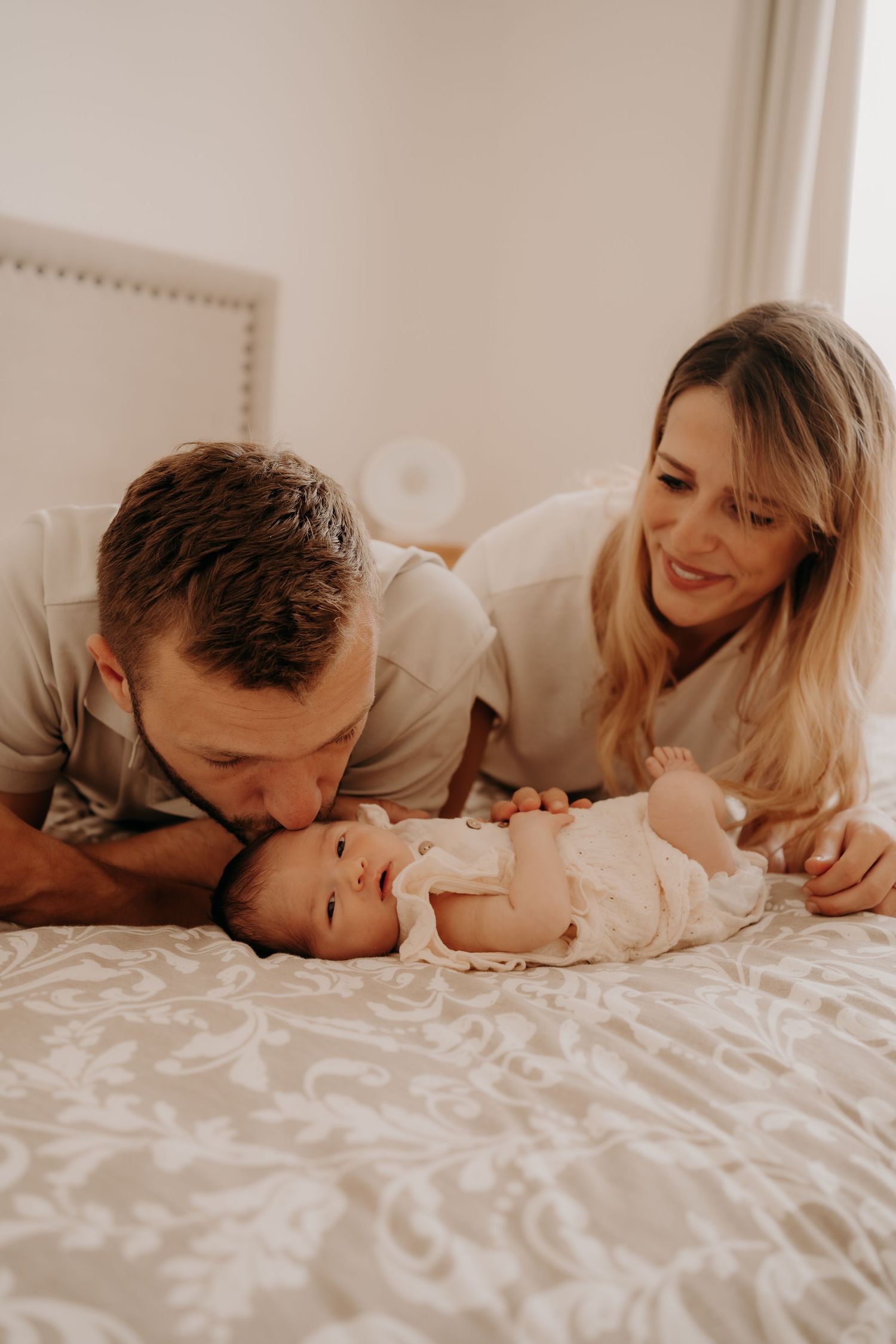 Family lying together on white bedding sharing sweet moments with their newborn.