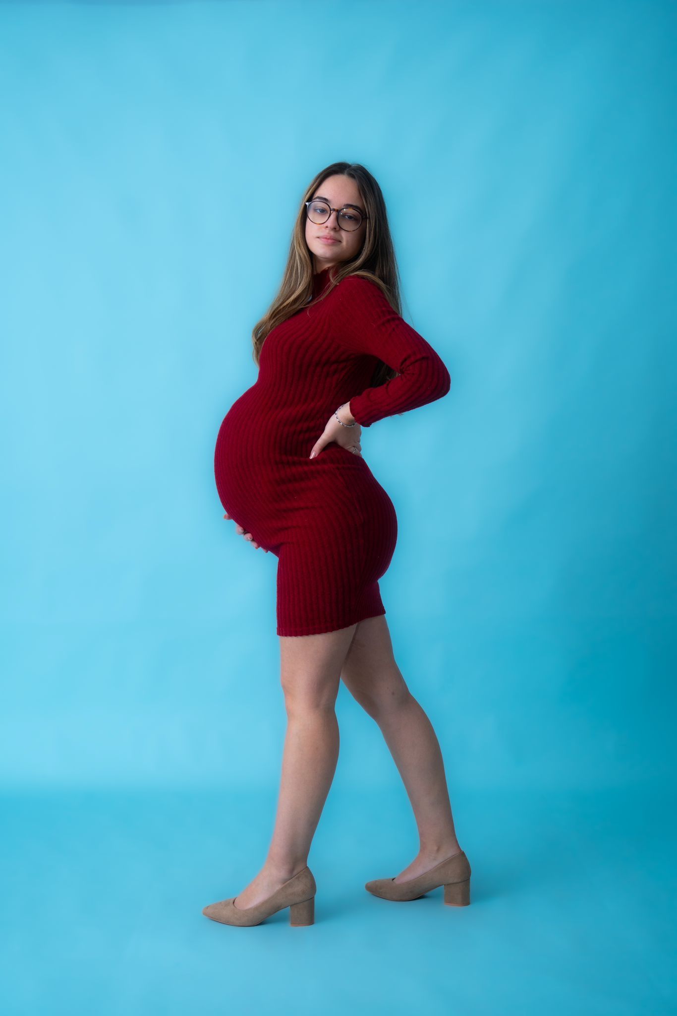 Woman in red sweater dress poses confidently against blue background.