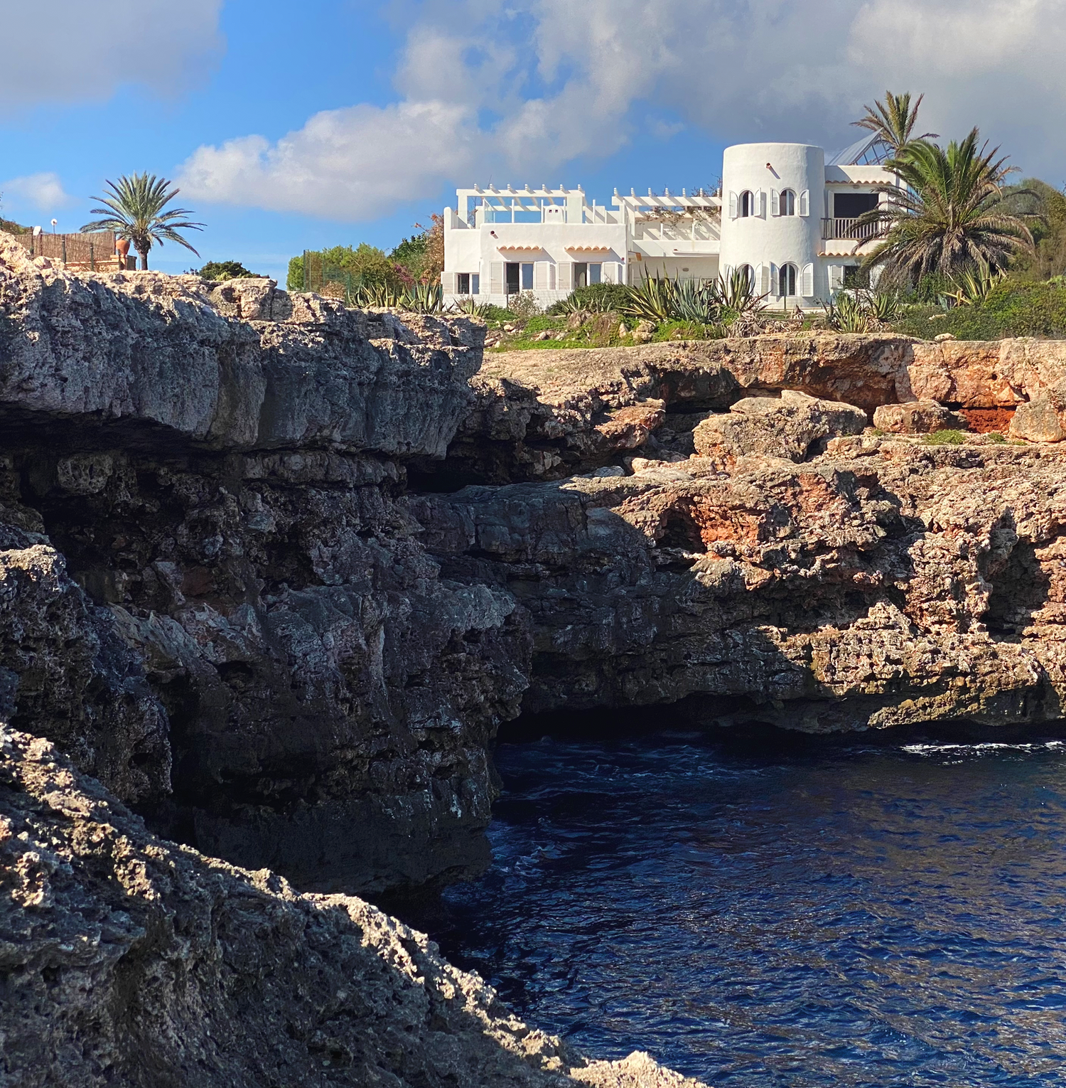 Luxurious white villa situated on rugged limestone cliffs with palm trees and ocean views.