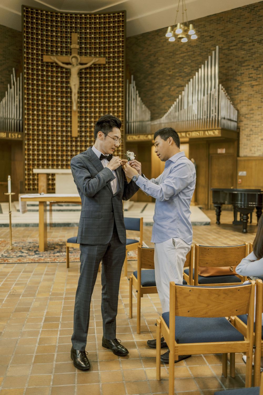 Two people lighting candles together in a church with crucifix and organ pipes in background.