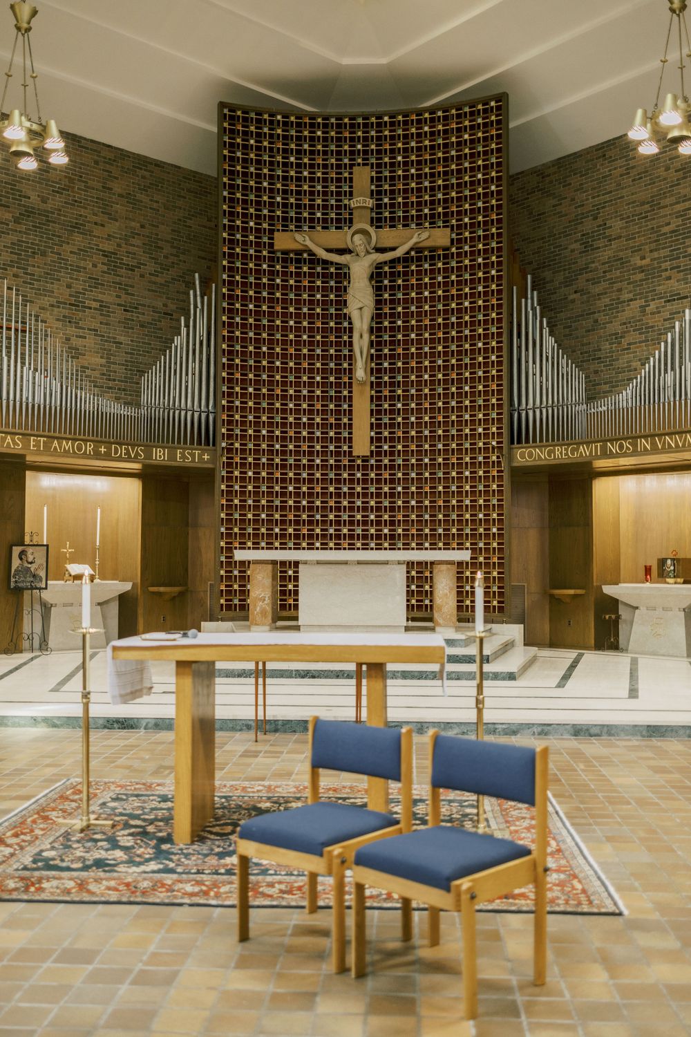 Modern church interior with large crucifix display and organ pipes against stone walls.