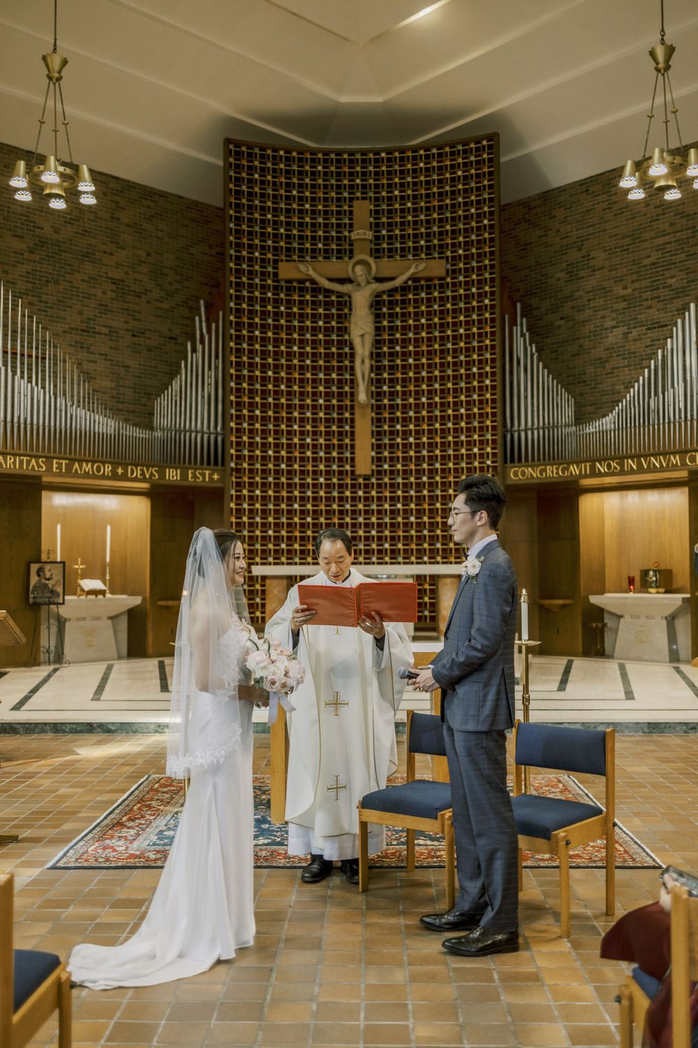 Wedding ceremony in progress at modern church with large crucifix and organ pipes visible.