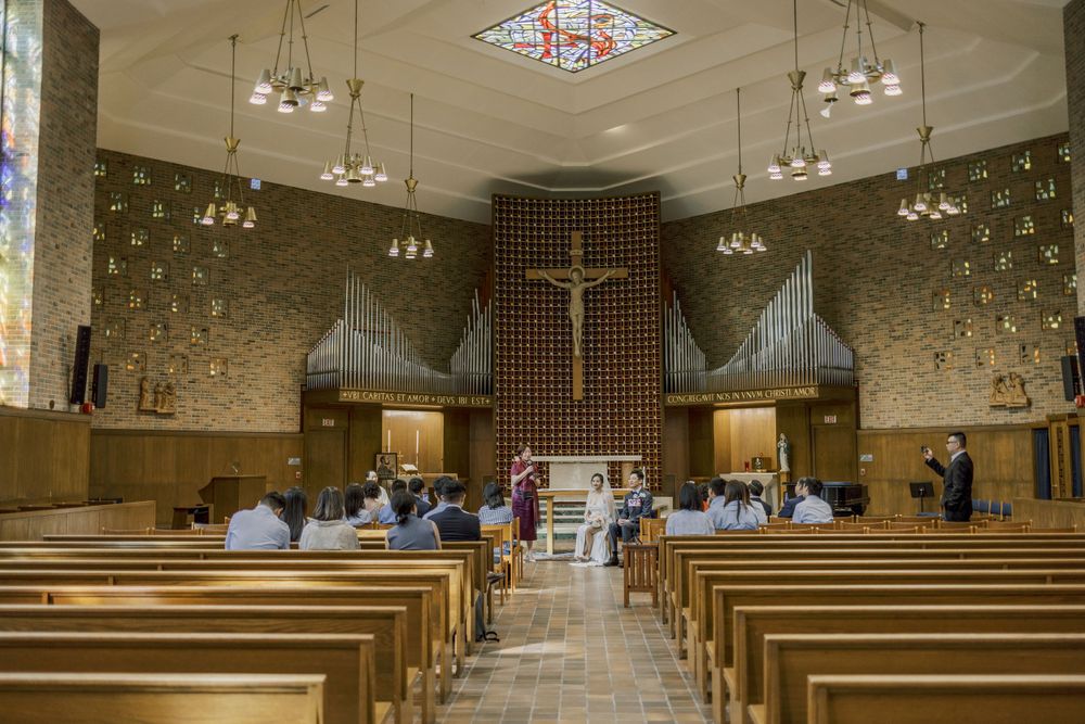 Modern church interior with rows of wooden pews, stained glass windows, and vaulted ceilings.