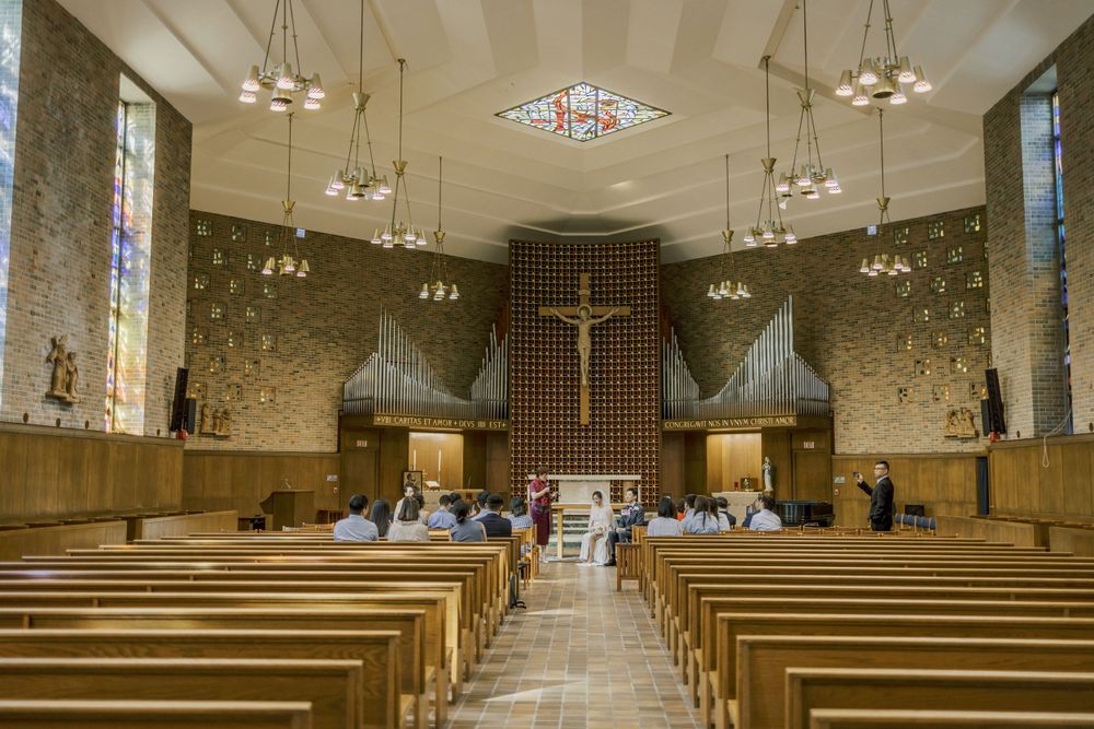 Church sanctuary with wooden pews, vaulted ceiling, and natural light streaming through stained glass windows.