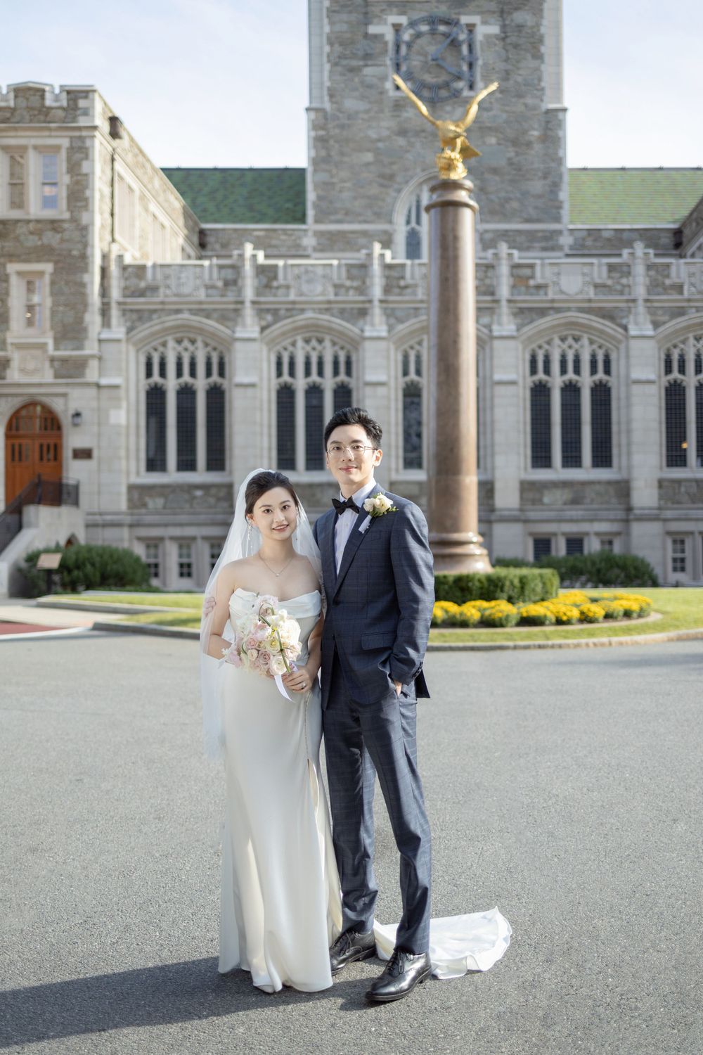 Wedding couple walking together outside a grand Gothic stone building with columns and architectural details.