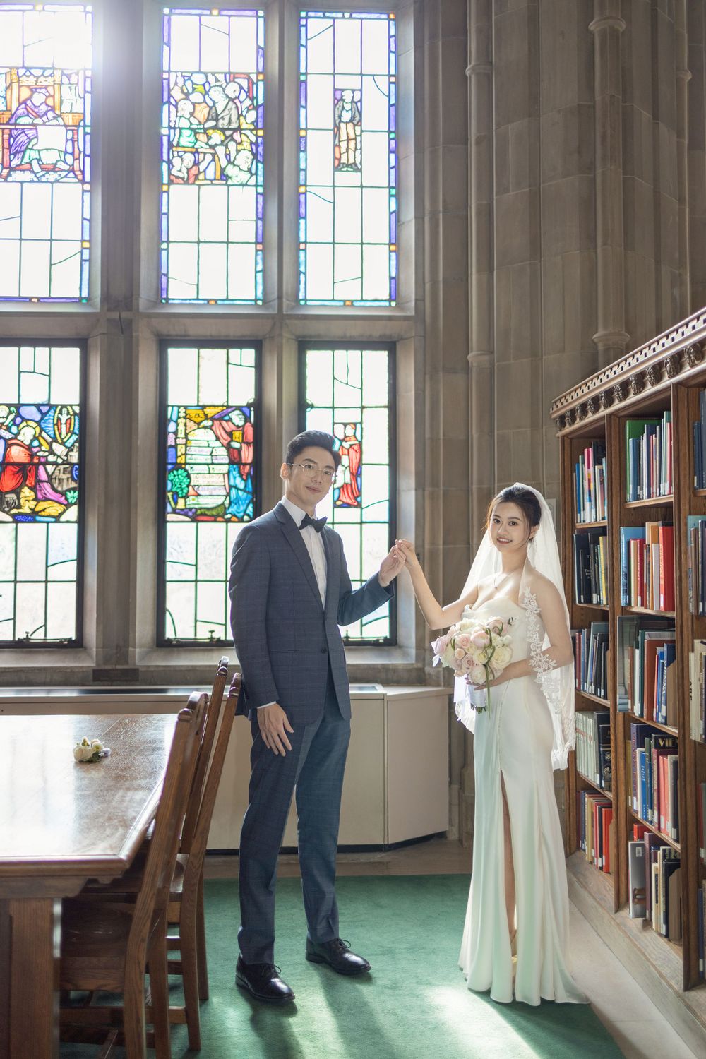 A couple sharing candid moments in a library with stained glass windows and bookshelves.
