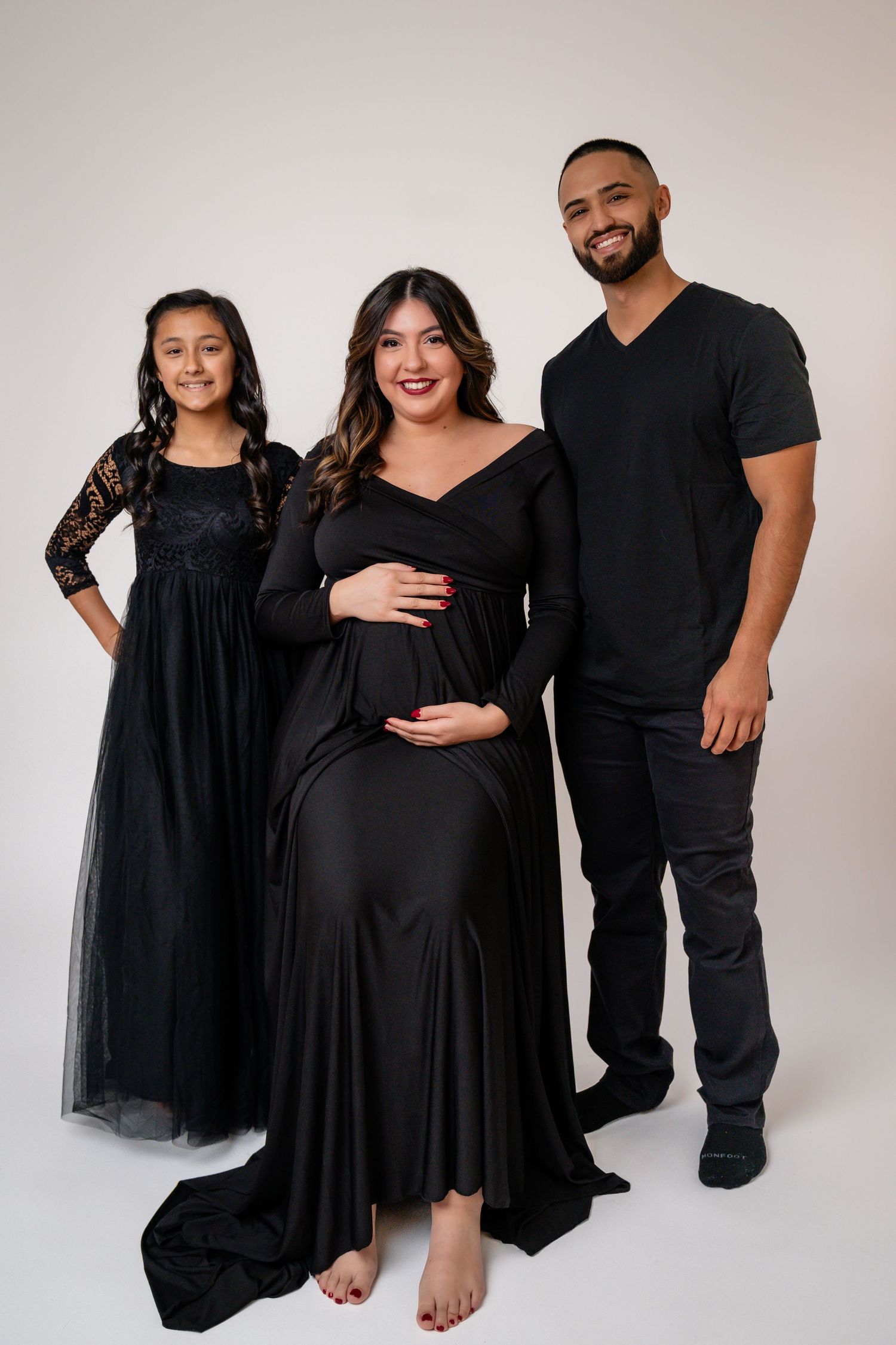 Family maternity portraits with matching black outfits against white studio background.