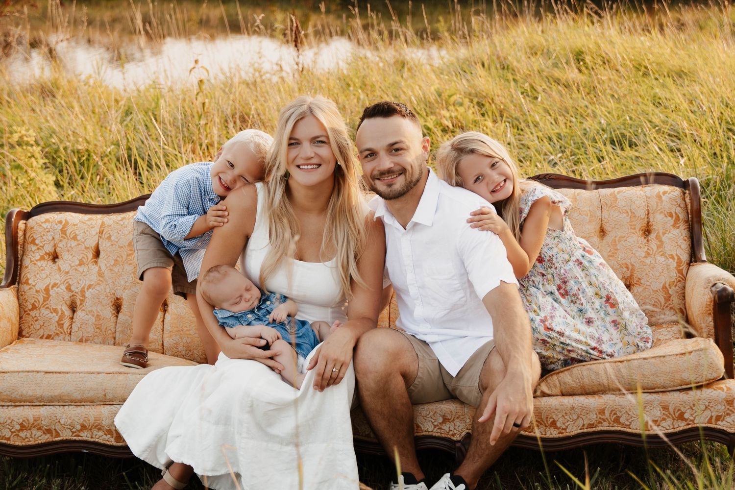 Family relaxing together on a vintage couch outdoors in a sunlit field. Family photo session.