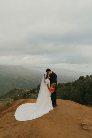 Wedding couple sharing an intimate moment on a mountain overlook with dramatic veil.