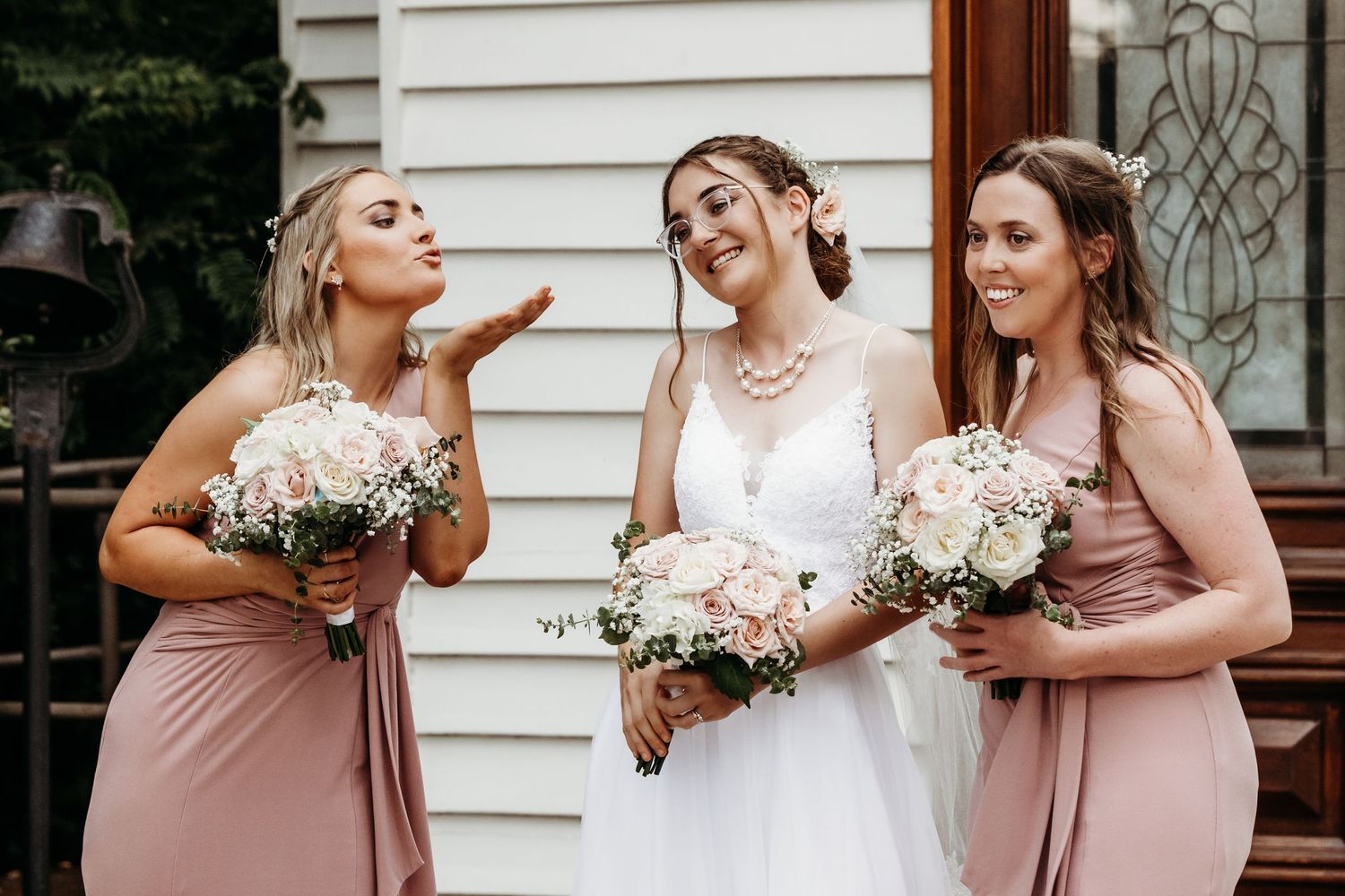 Three bridesmaids share a candid laughing moment while holding white floral bouquets.