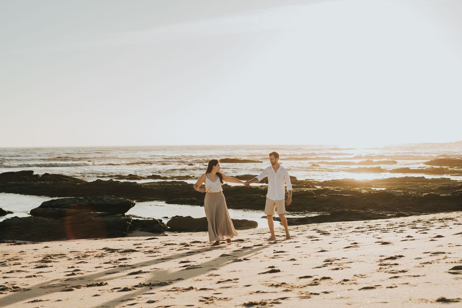 Couple walking on rocky beach during golden sunset hour.