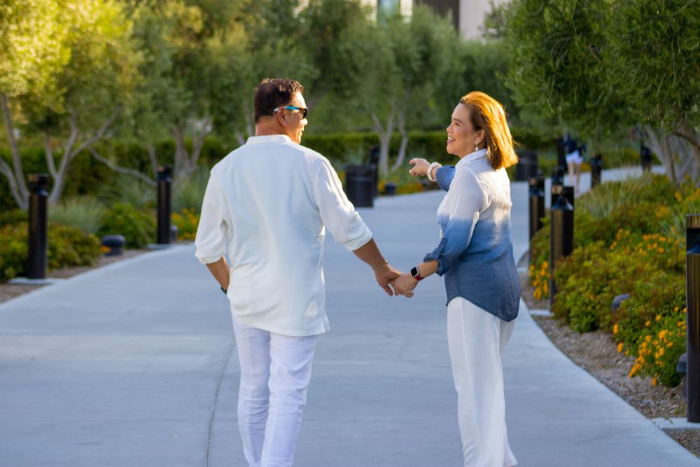 Couple holding hands walking along a sunny garden pathway in matching white and blue outfits.