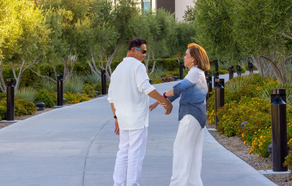 A couple dances playfully on a scenic garden pathway surrounded by colorful flowers and trees.