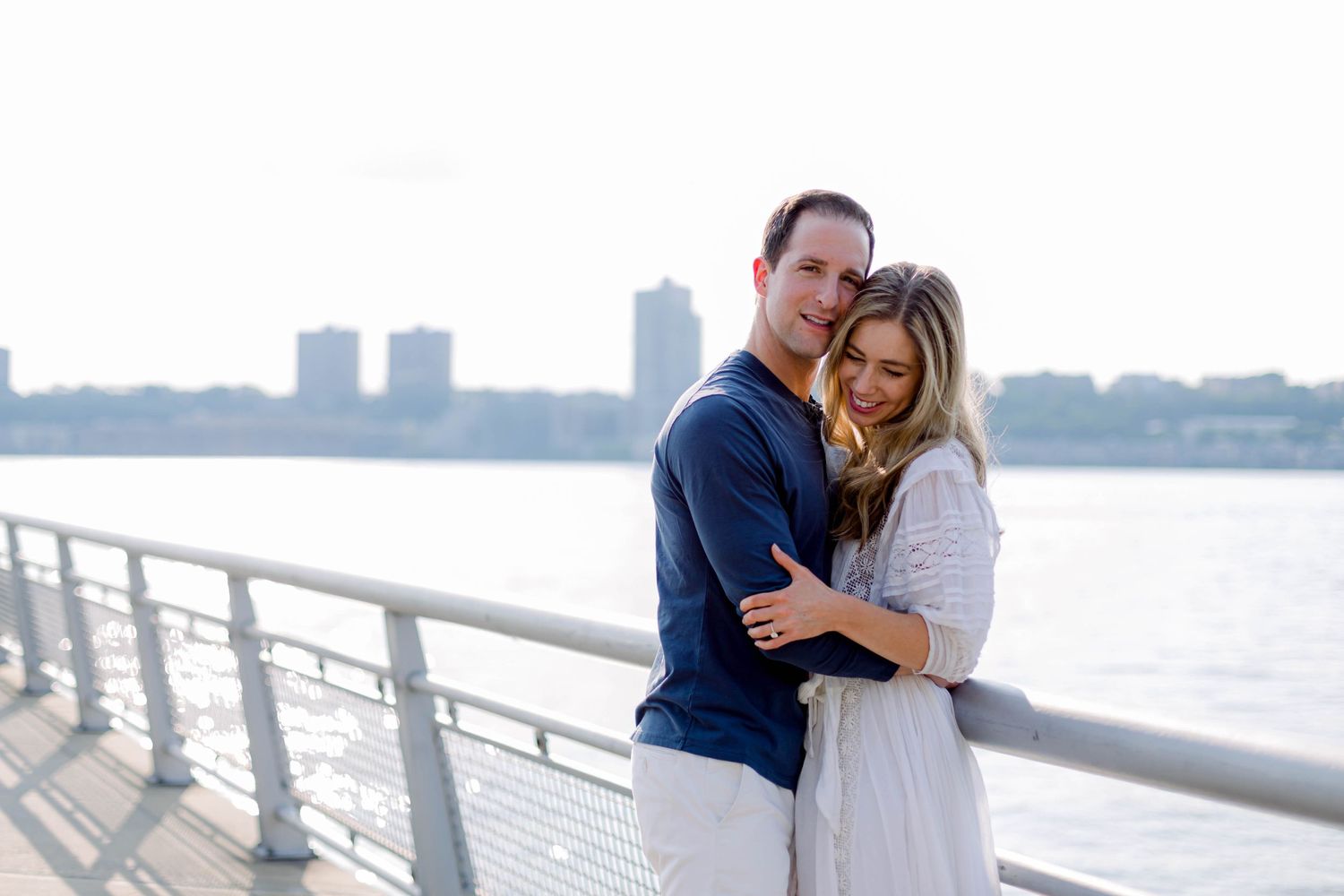 A tender embrace along a waterfront with city skyline in the background.