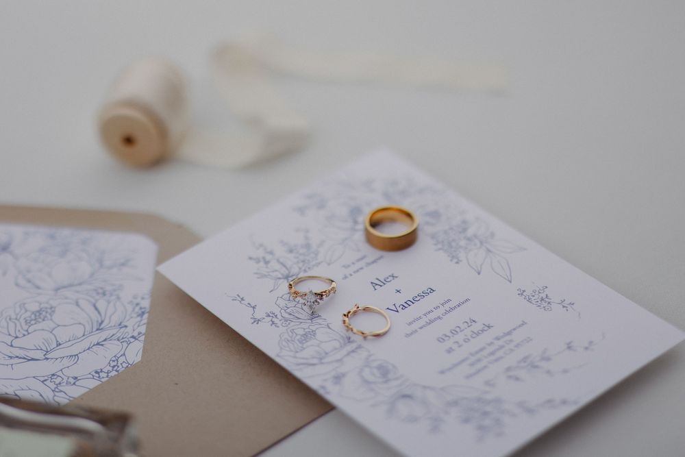 Wedding rings and invitation with delicate floral details displayed on white paper.