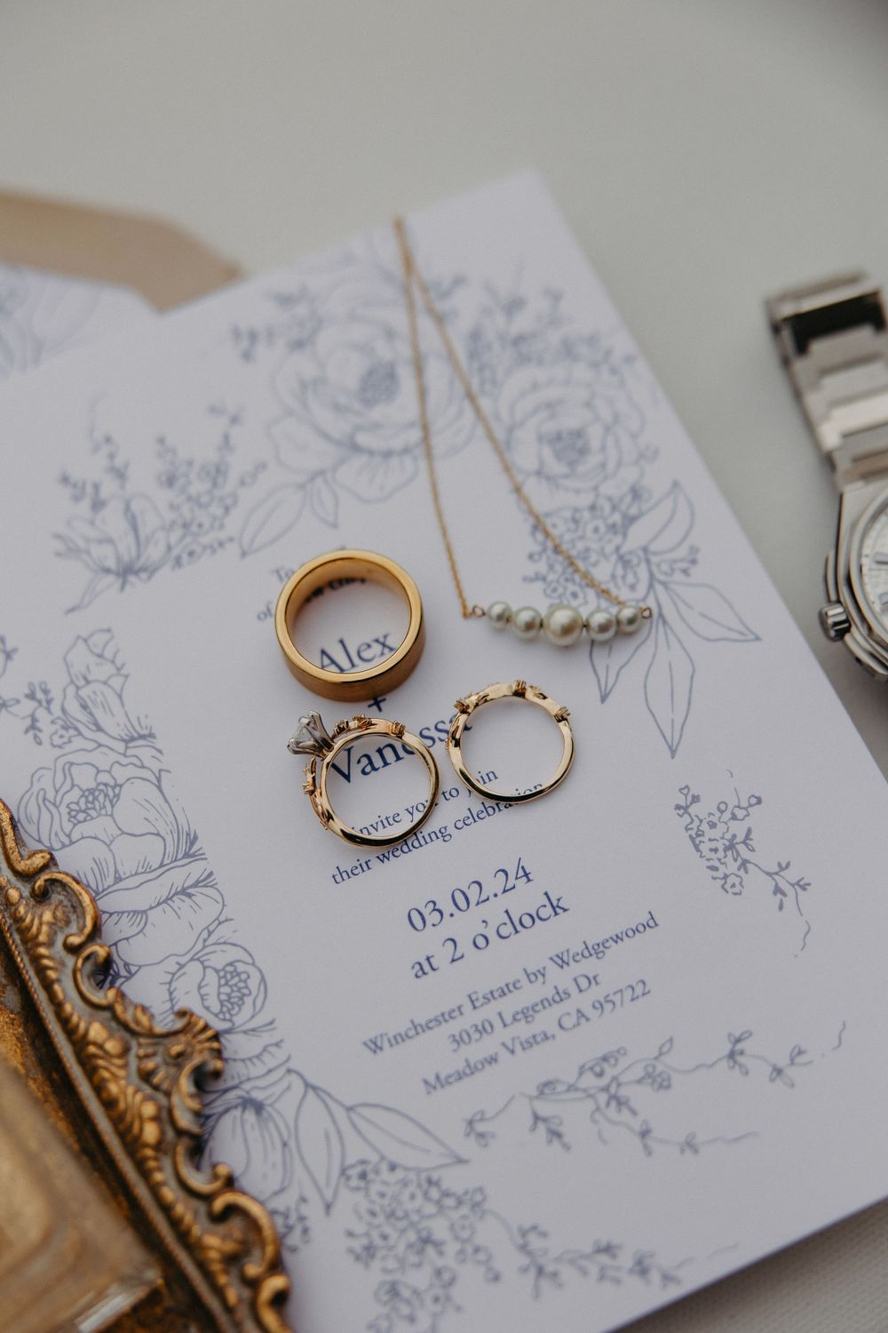 Wedding jewelry and rings arranged on a delicate floral wedding invitation.